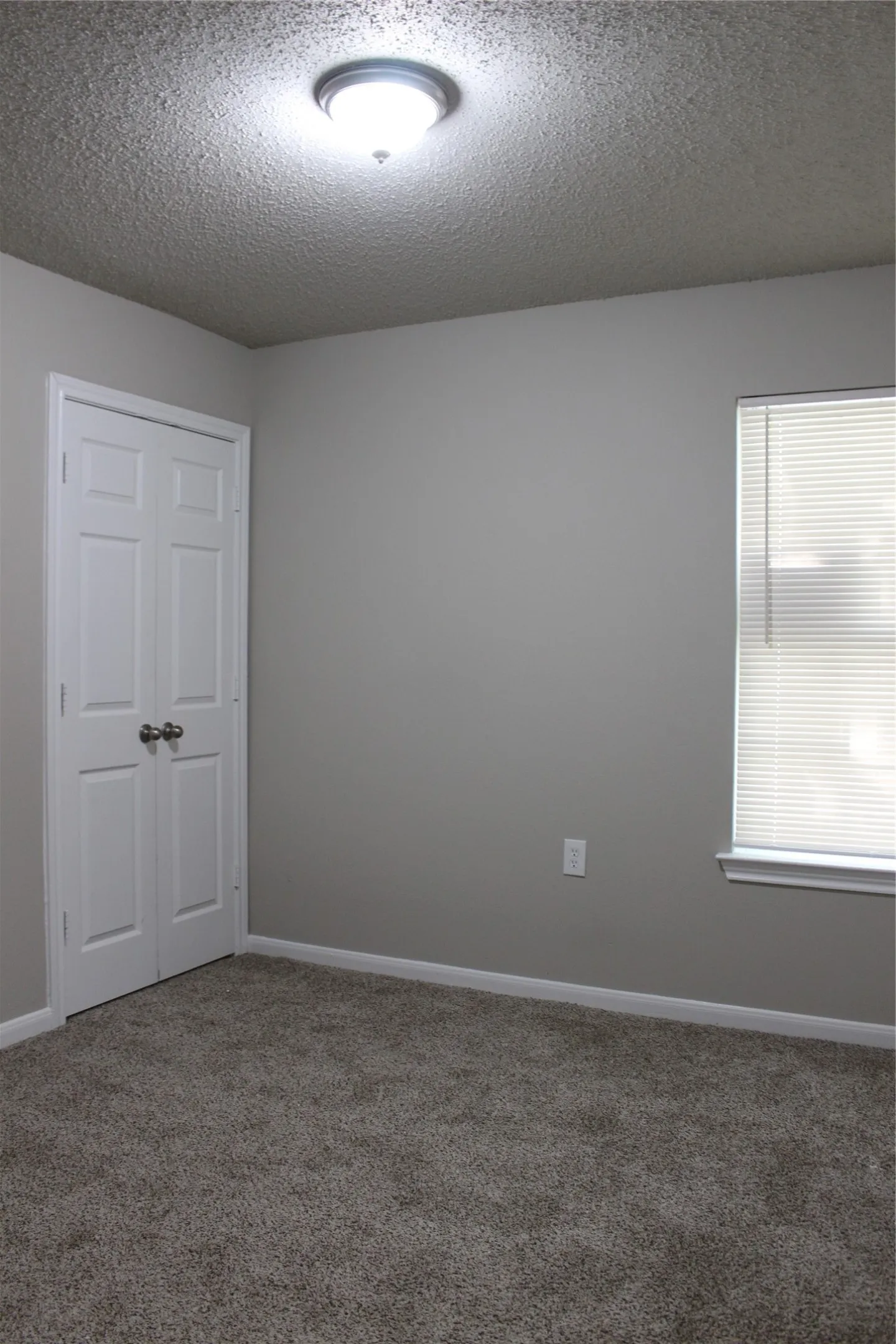 Neutral wall paint, textured ceiling, double-panel closet doors, wall-to-wall carpeting, and a window with blinds