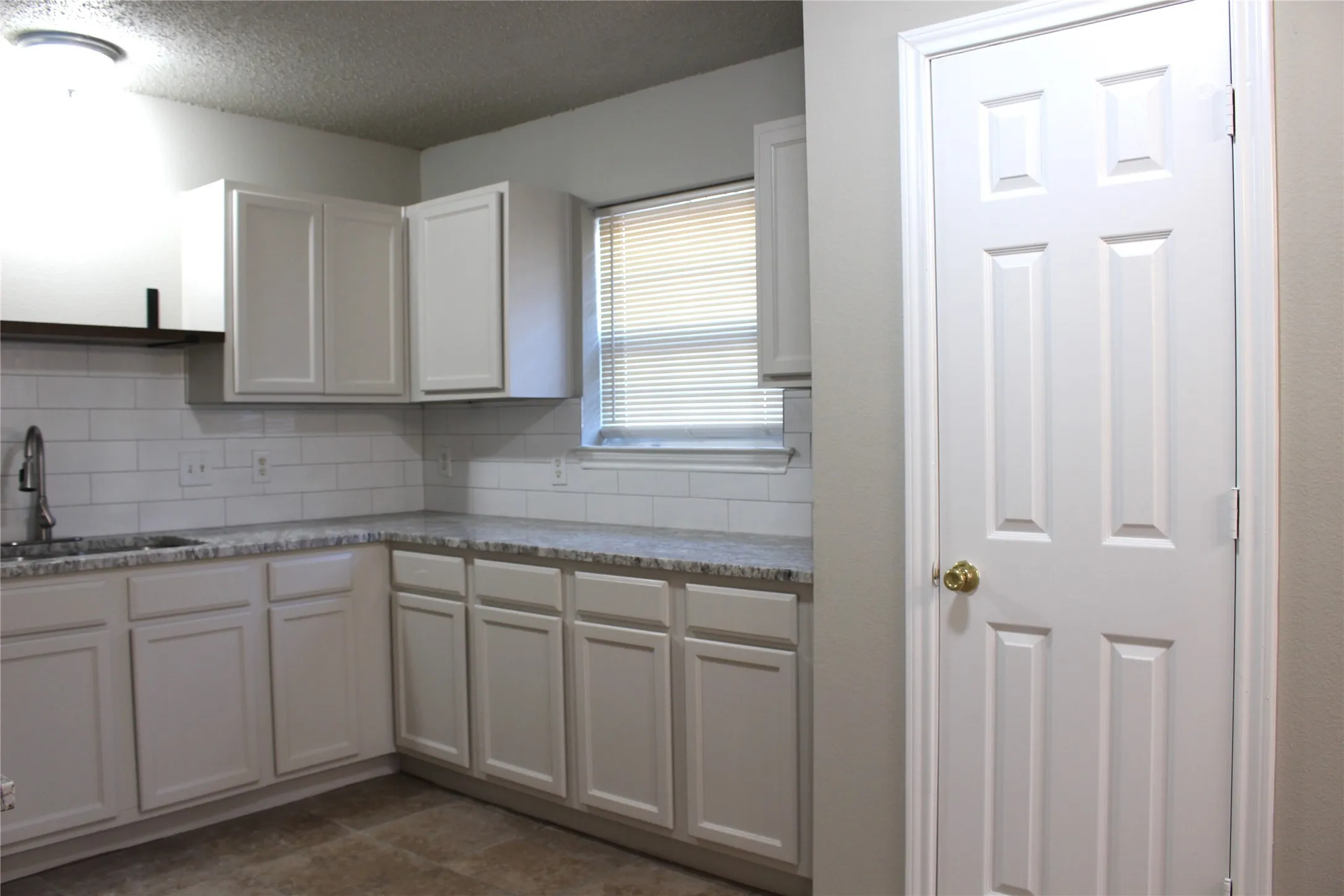 Kitchen featuring white cabinetry, subway tile backsplash, light-toned countertops, a stainless steel sink, and tile flooring