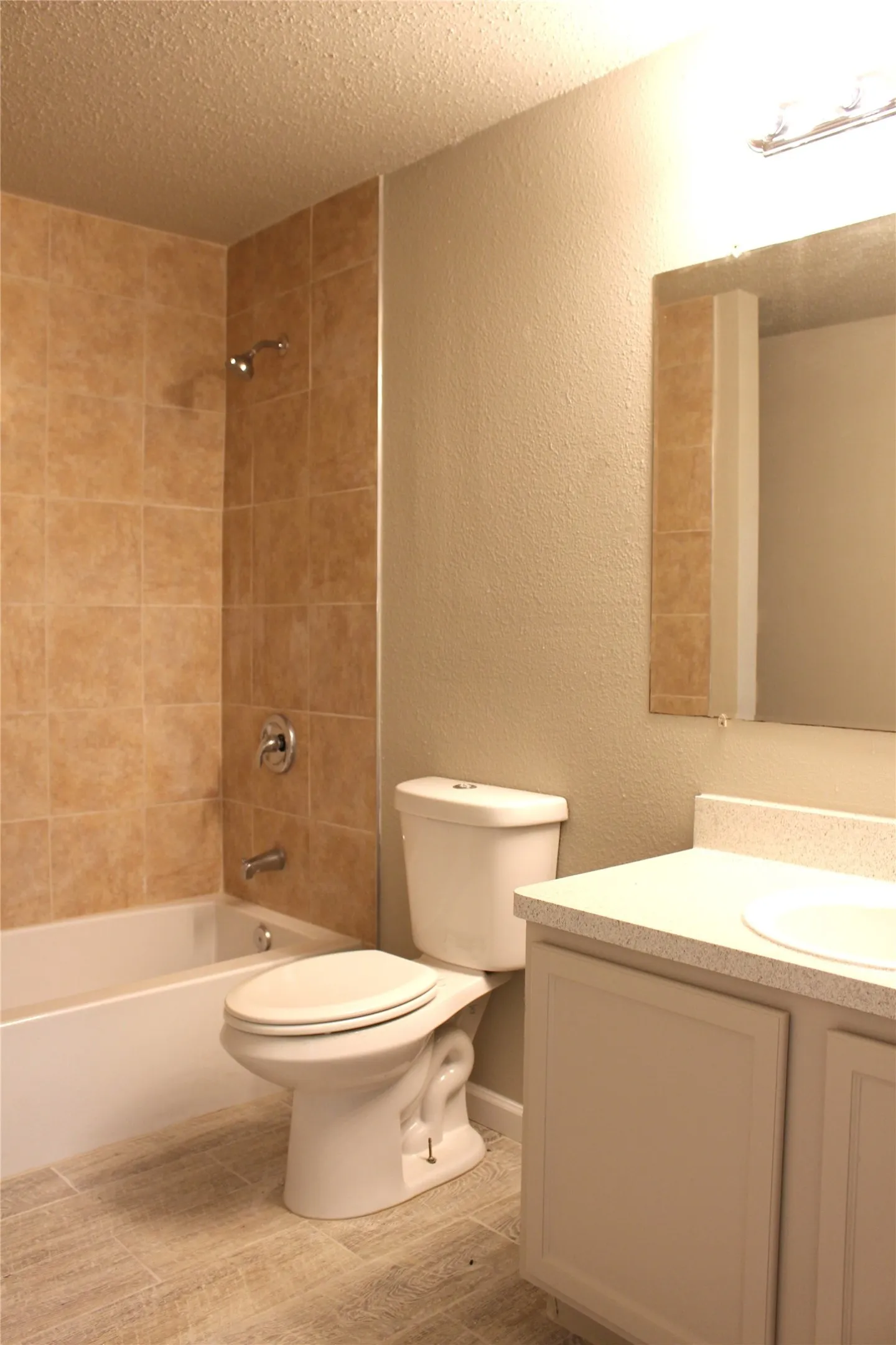 Bathtub with tile surround, white vanity, integrated sink, and plank-style floor tiles