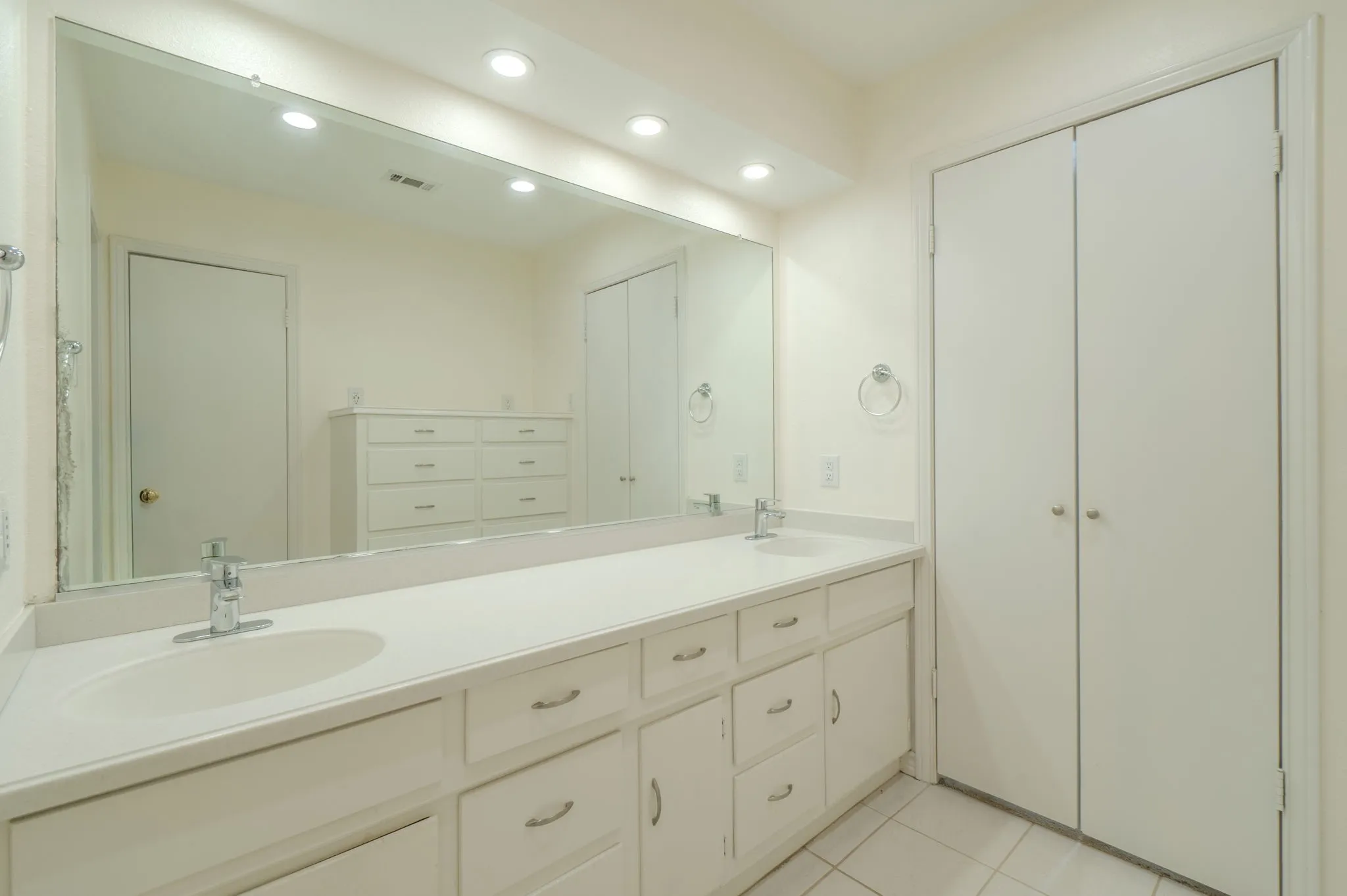 Dual vanity with integrated sinks, expansive wall-mounted mirror, recessed lighting, and white cabinetry with silver-toned hardware