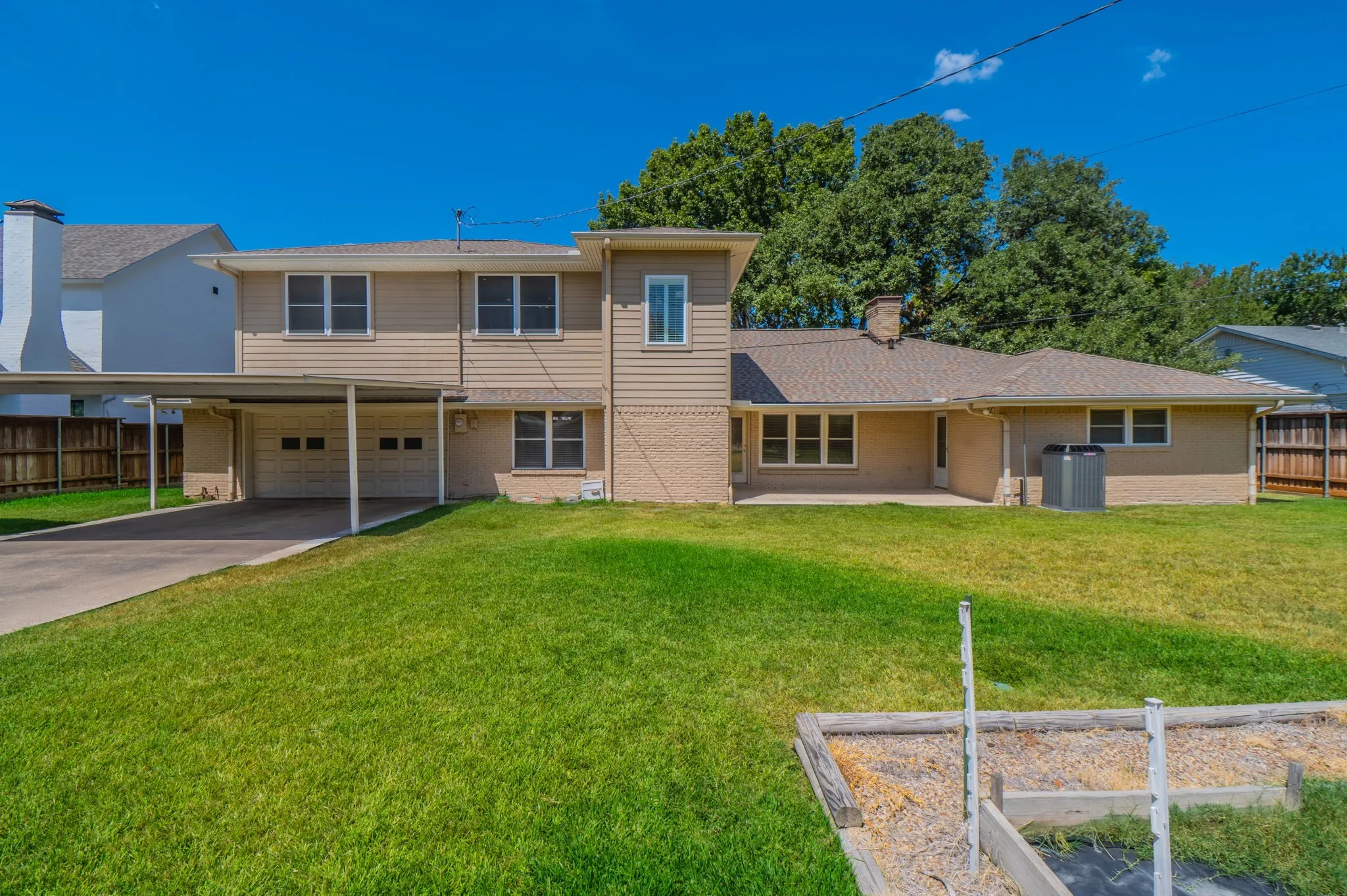 Carport with a two-car garage, brick and siding exterior, multiple windows, and a paved patio area