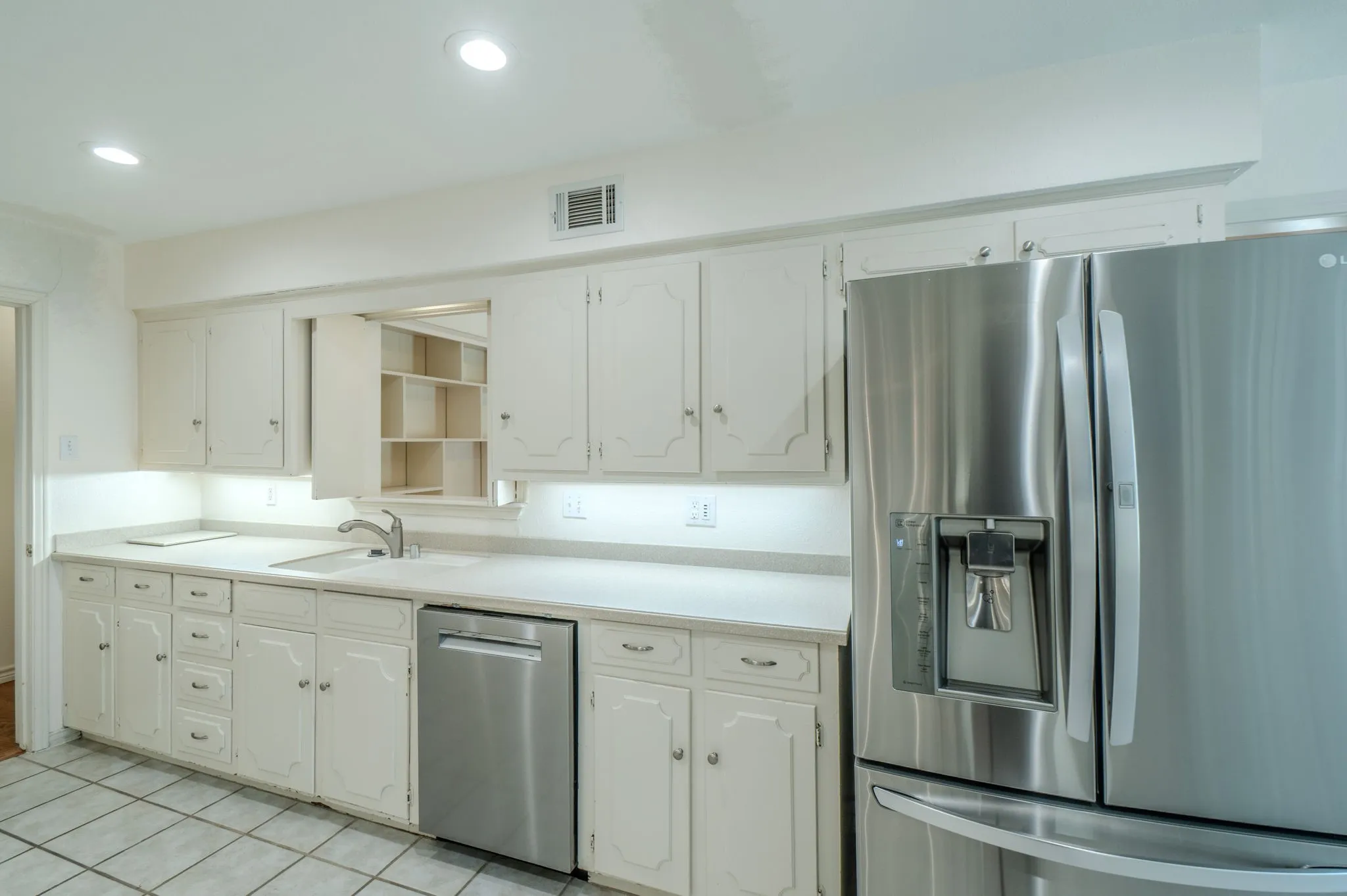 White cabinetry with under-cabinet lighting, stainless steel appliances, and a tiled floor
