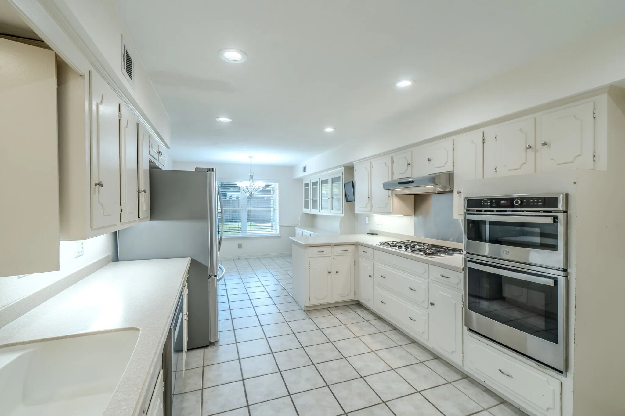 Kitchen featuring white cabinetry, light countertops, integrated dual wall ovens, a gas cooktop with exhaust hood, and recessed lighting