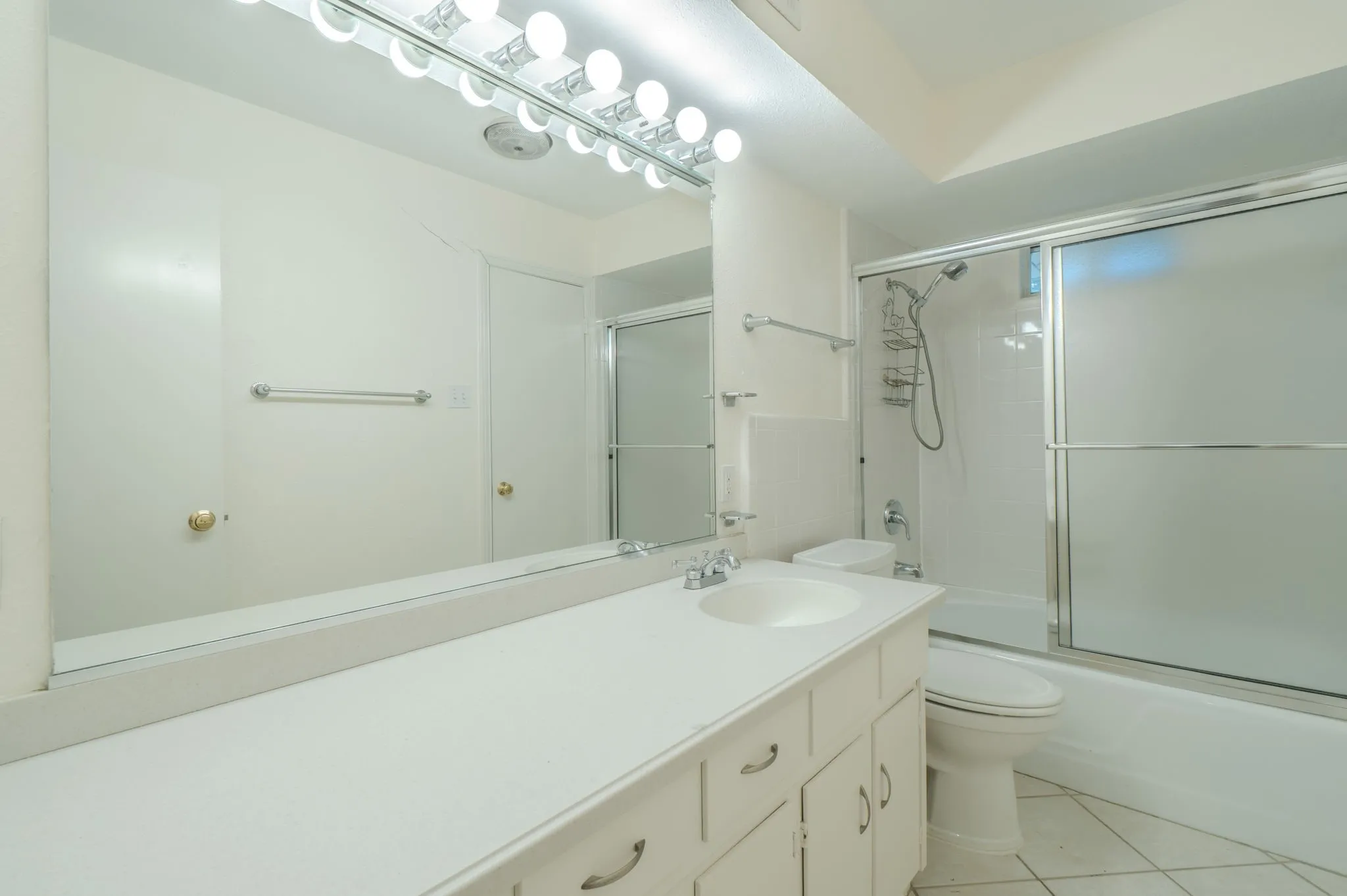 White vanity with integrated sink, chrome faucet, and expansive wall mirror with vanity lighting
