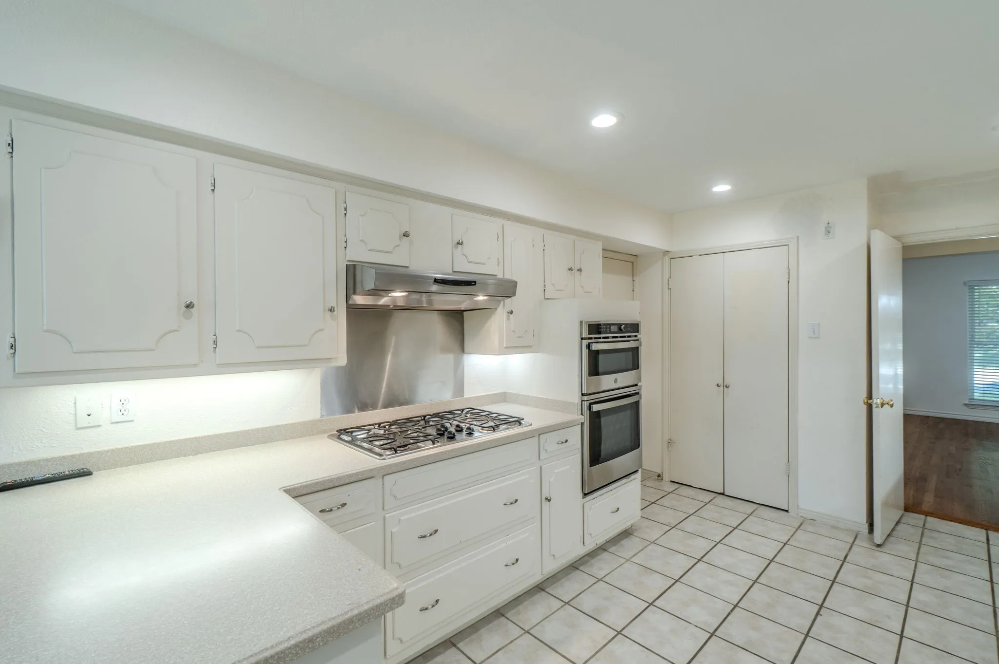 White cabinetry with decorative door panels, stainless steel gas cooktop, stainless steel double wall ovens, recessed lighting, and tile flooring