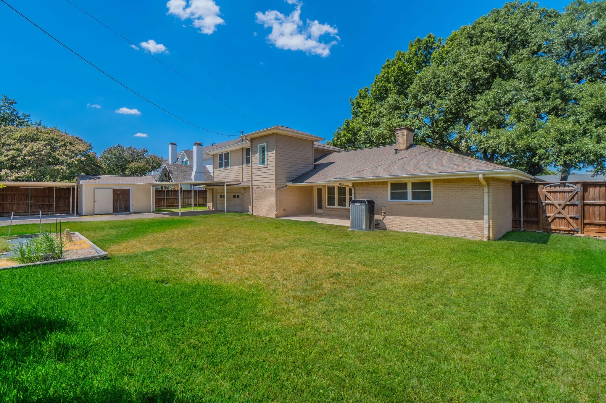 Expansive backyard featuring a manicured lawn, brick and siding exterior, a covered walkway, and mature trees Building w/ elec great shop or storage