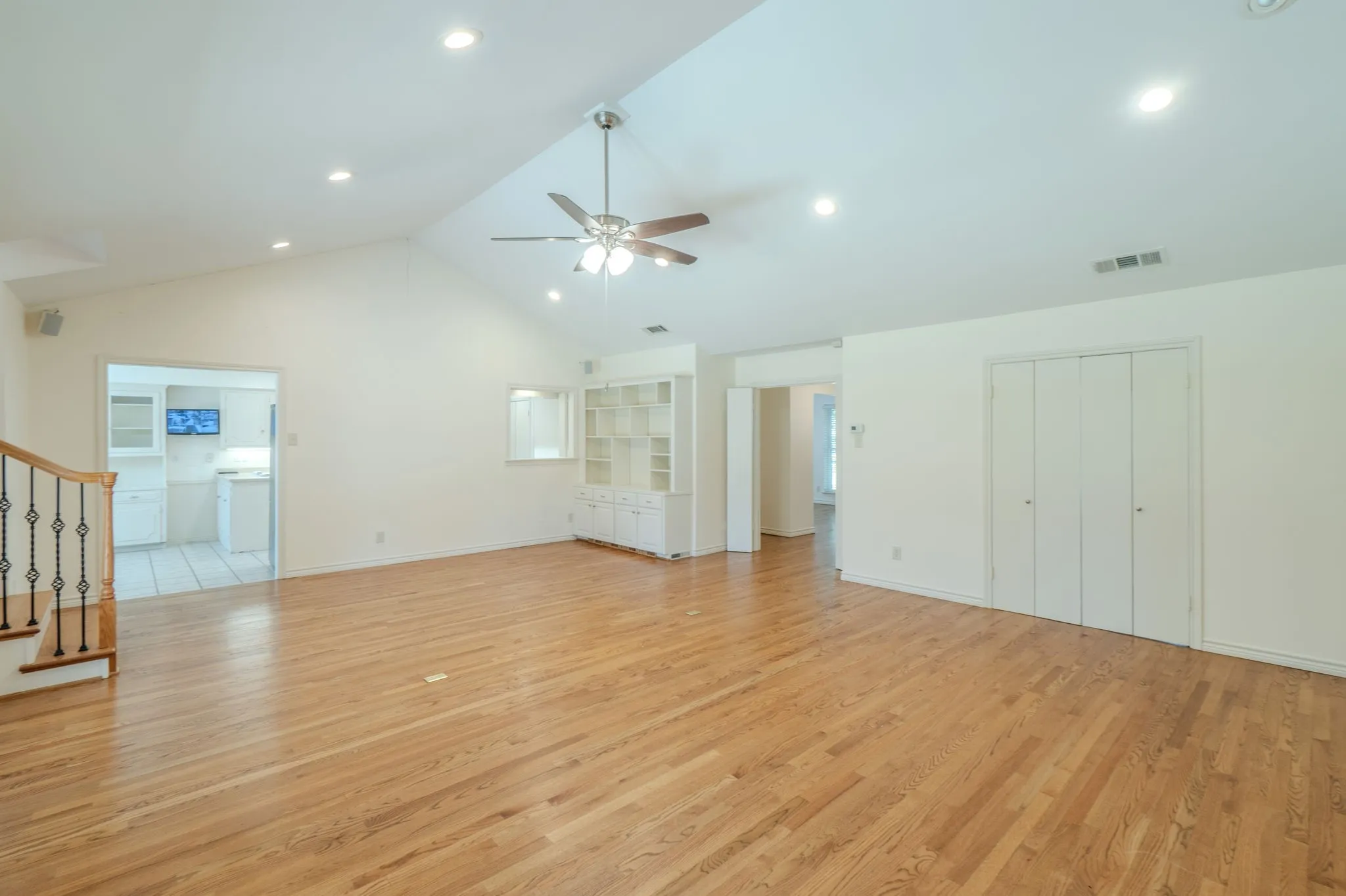Vaulted ceiling with recessed lighting, wood-finish flooring, ceiling fan with integrated lighting, built-in shelving, and bi-fold closet doors