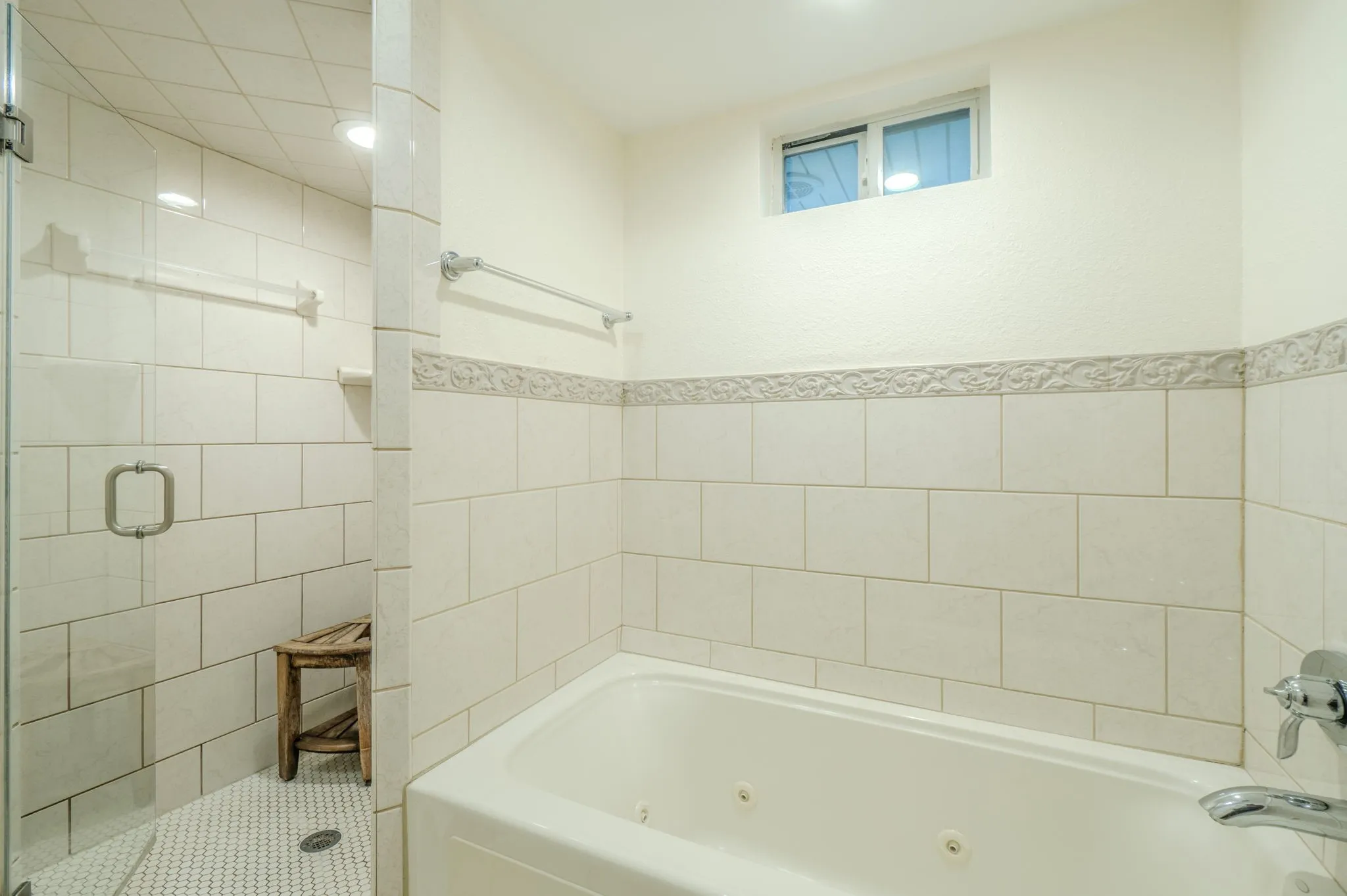 Tiled shower with glass enclosure, white rectangular wall tiling with decorative trim, and an integrated jetted tub