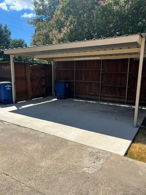 Covered carport with concrete flooring, wood privacy fencing, and a side access ^ car total gate
