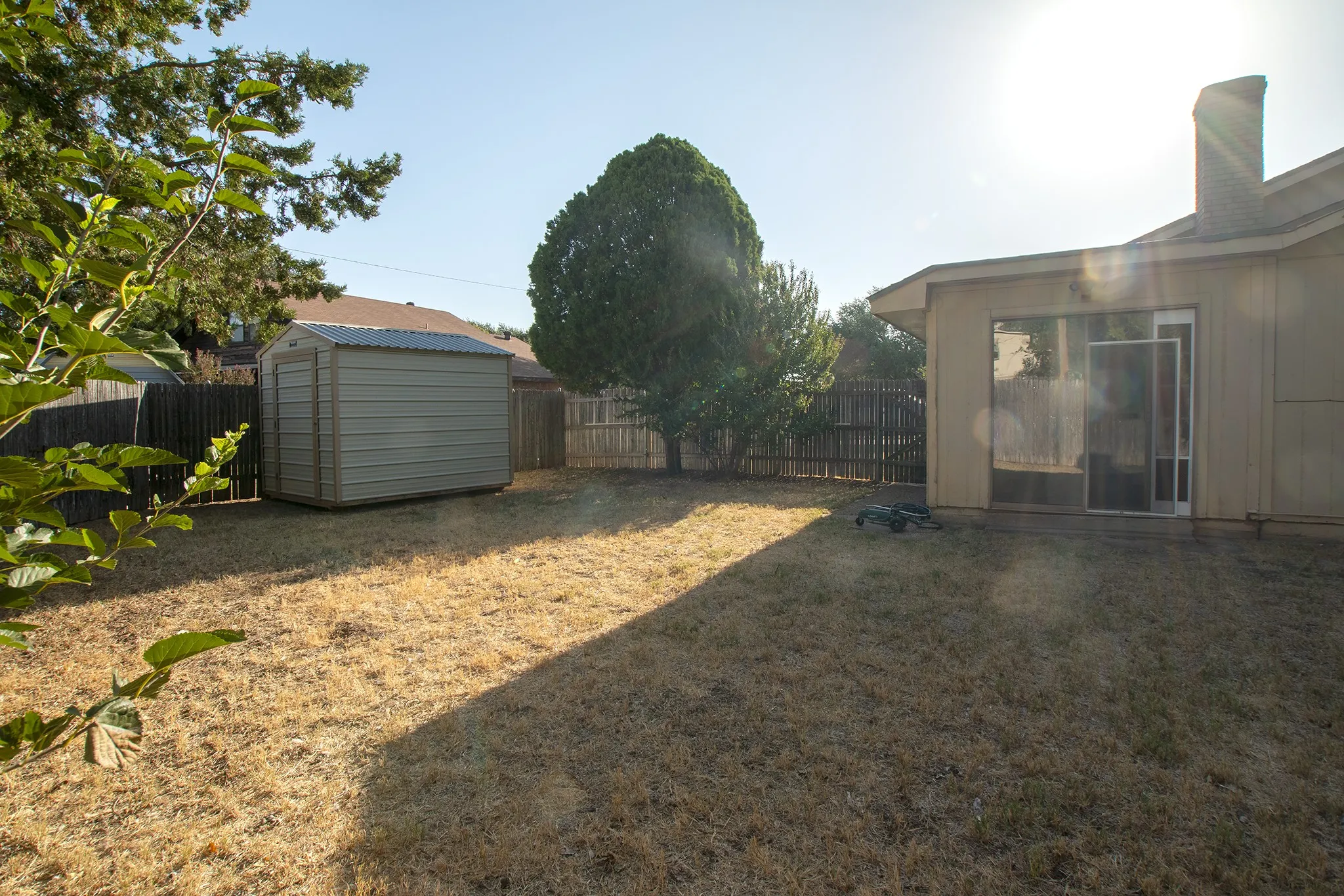 Expansive backyard featuring a metal shed, wood fencing, and a sliding glass door