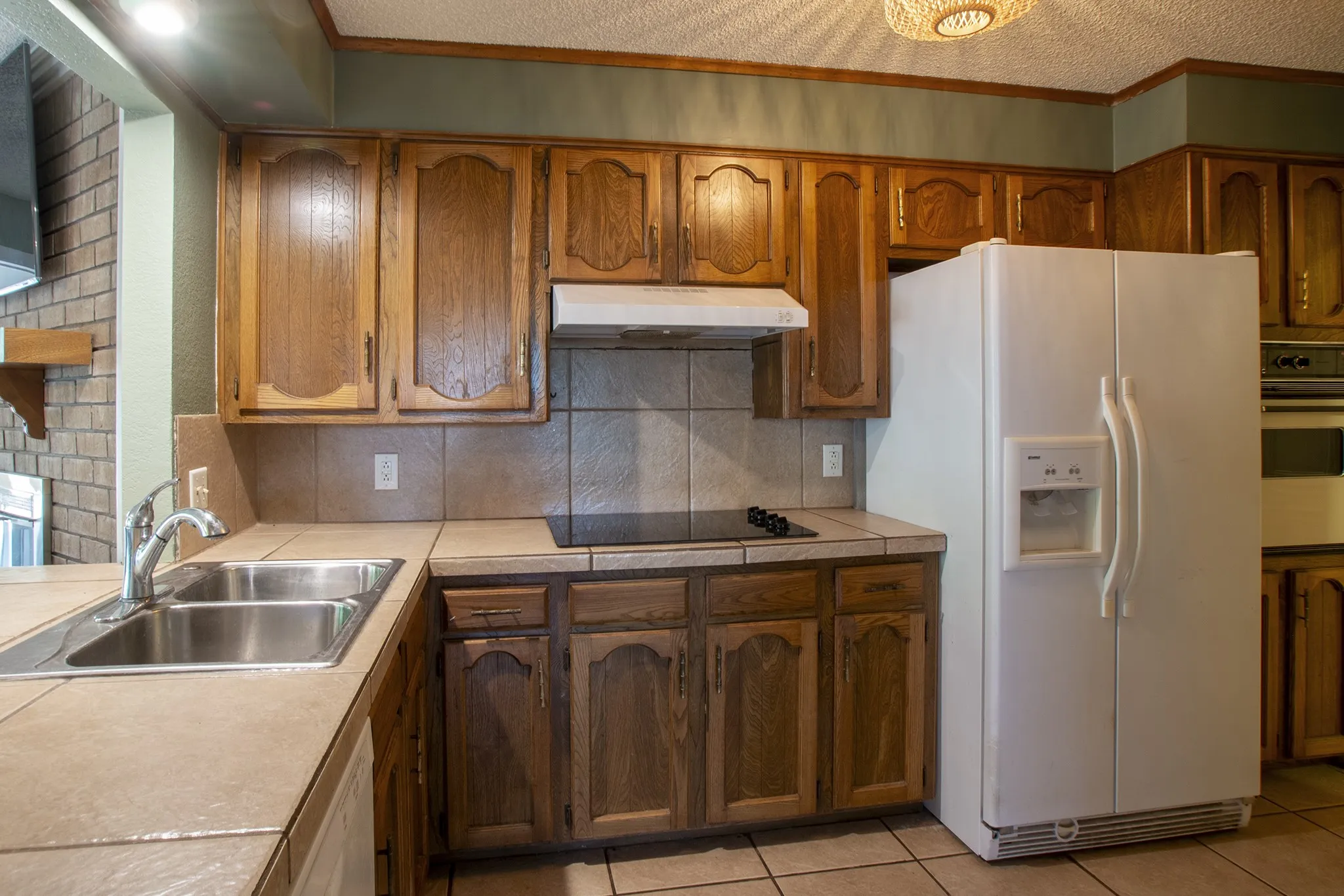 Kitchen featuring wood cabinetry, tile countertops, stainless steel double basin sink, and a built-in cooktop