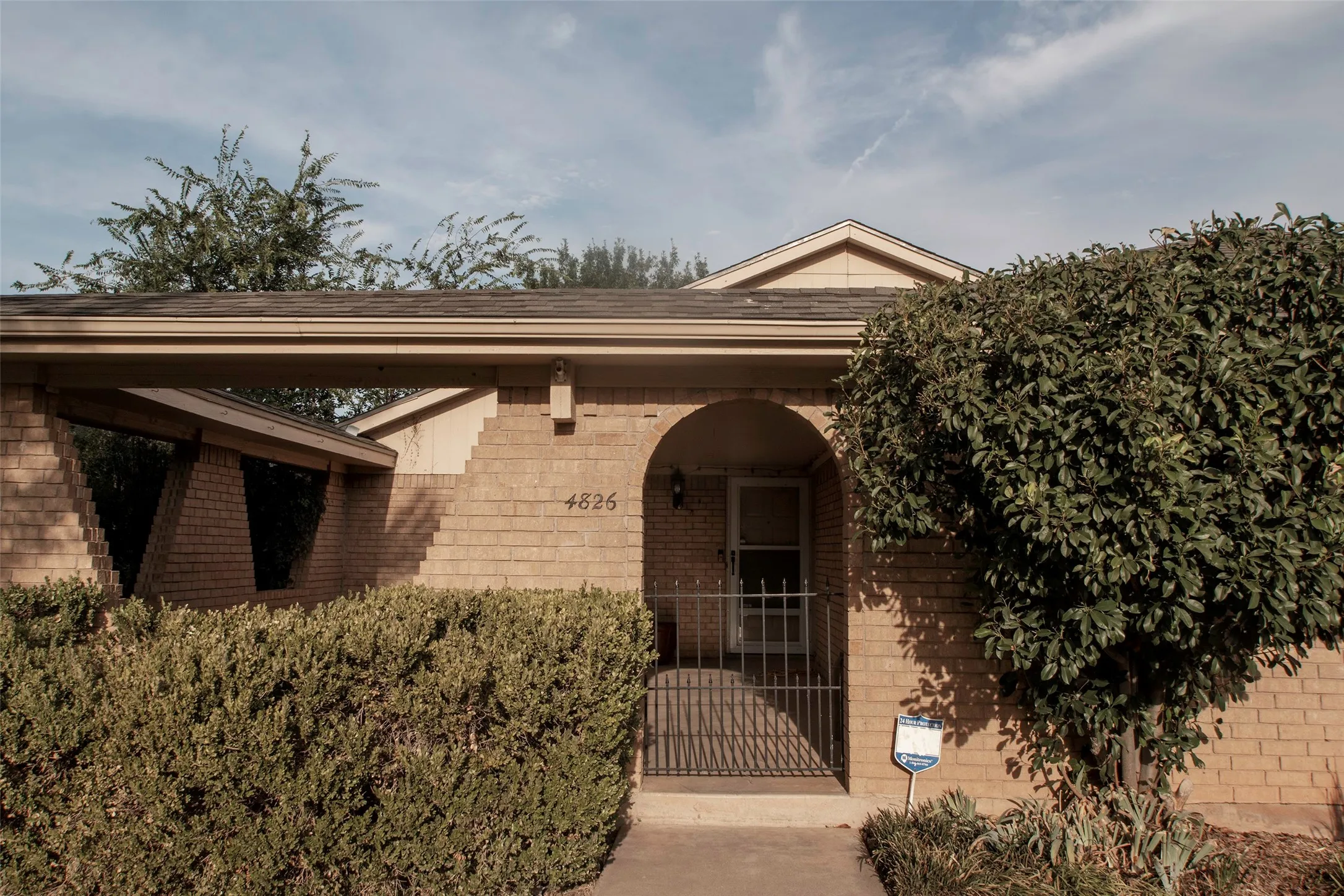 Brick exterior with a covered entry, arched doorway, and mature shrubbery