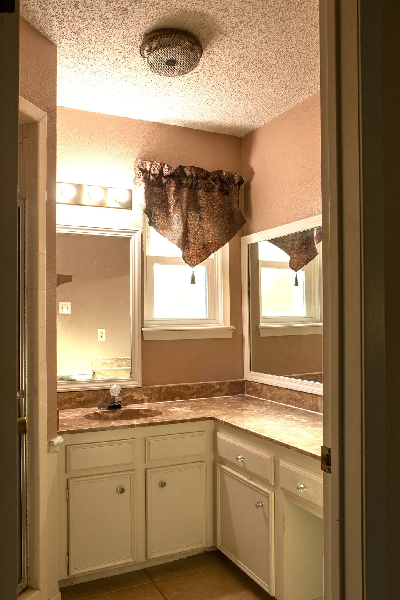 White painted cabinetry with knob hardware, L-shaped countertop, integrated sink, and wall-mounted mirrors