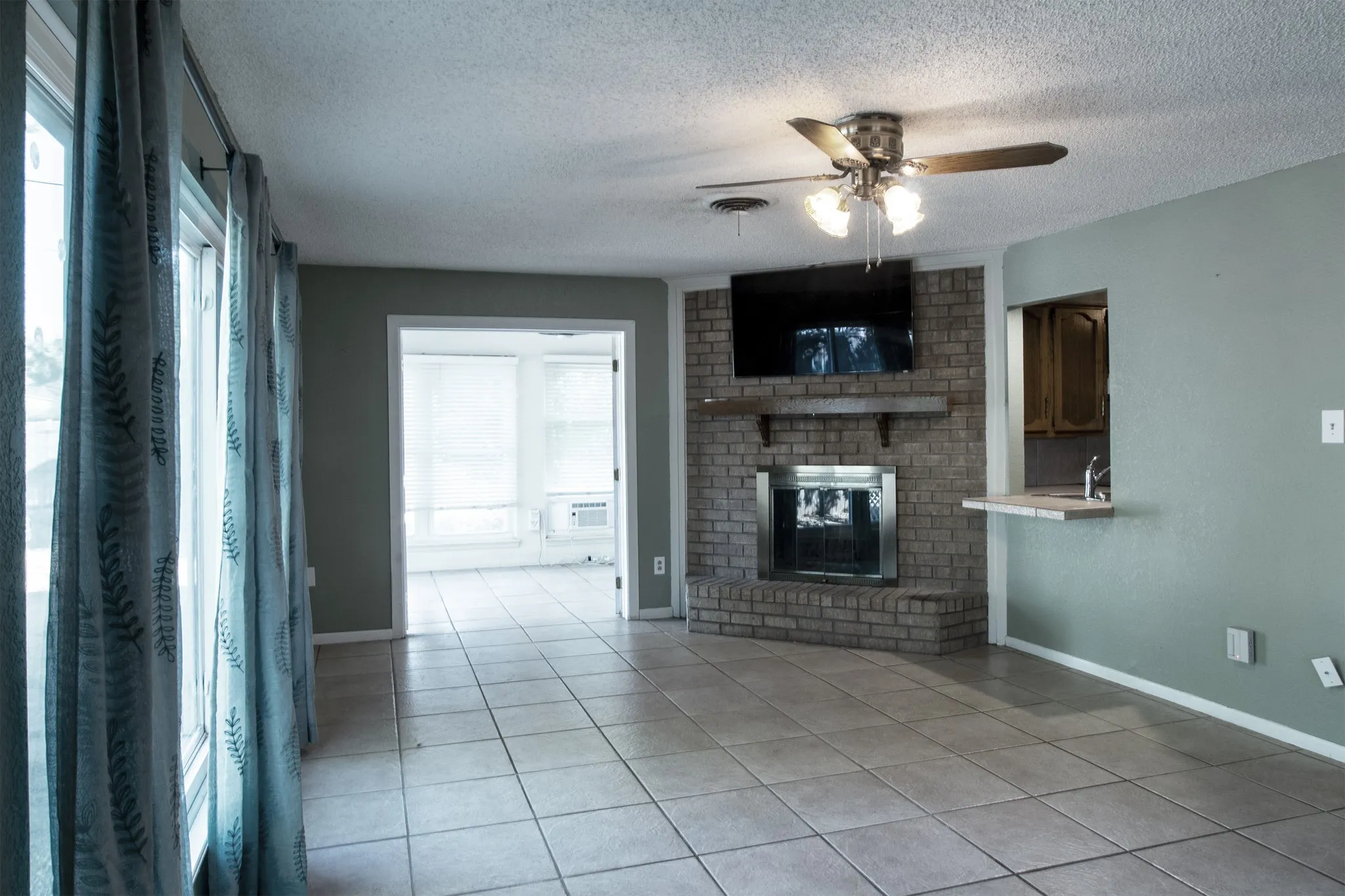 Living area featuring tile flooring, a brick fireplace with a wood mantel, an integrated breakfast bar, and a ceiling fan with integrated lighting