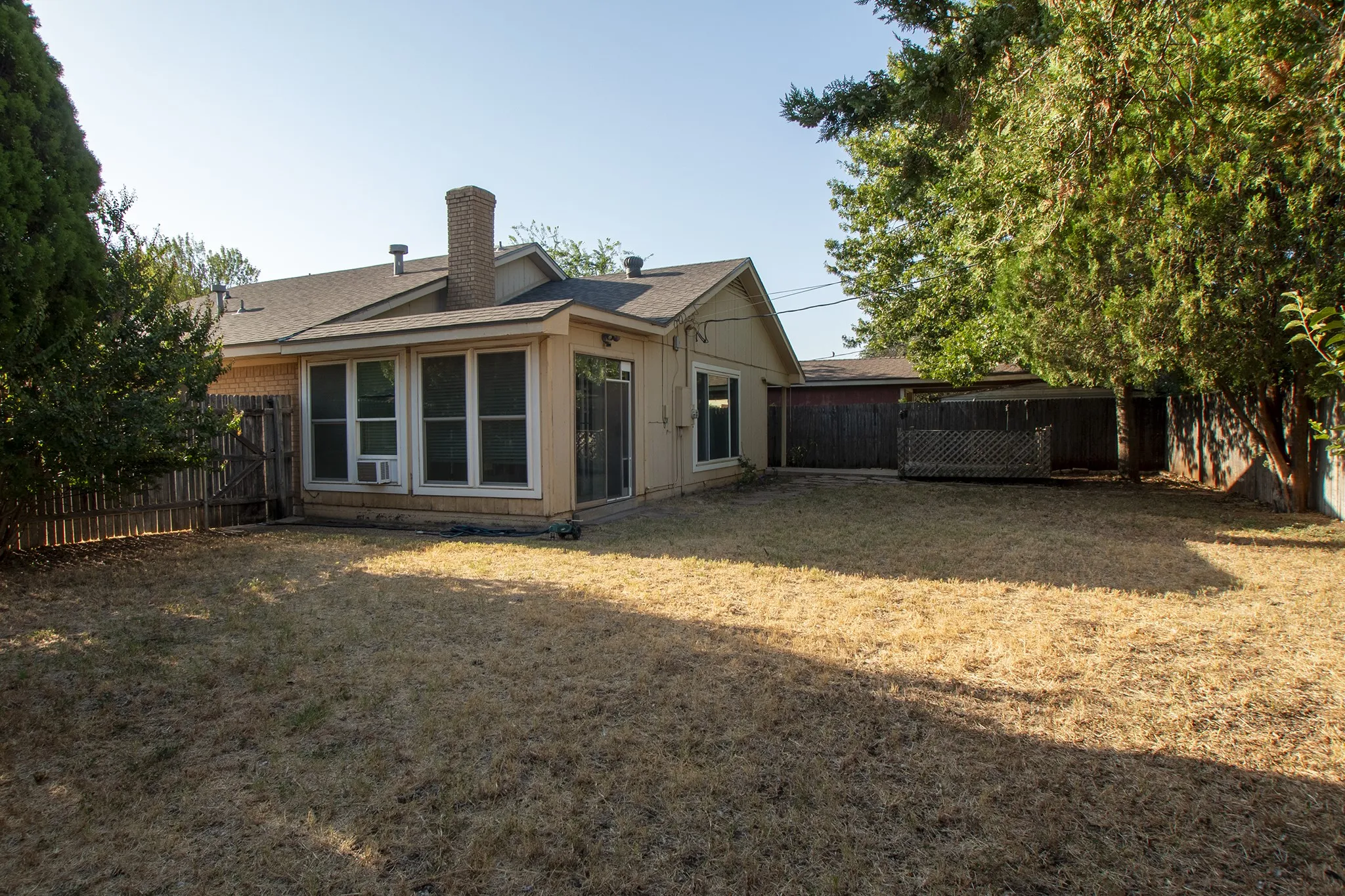Expansive backyard featuring a wood privacy fence, mature trees, and a ground-level deck structure