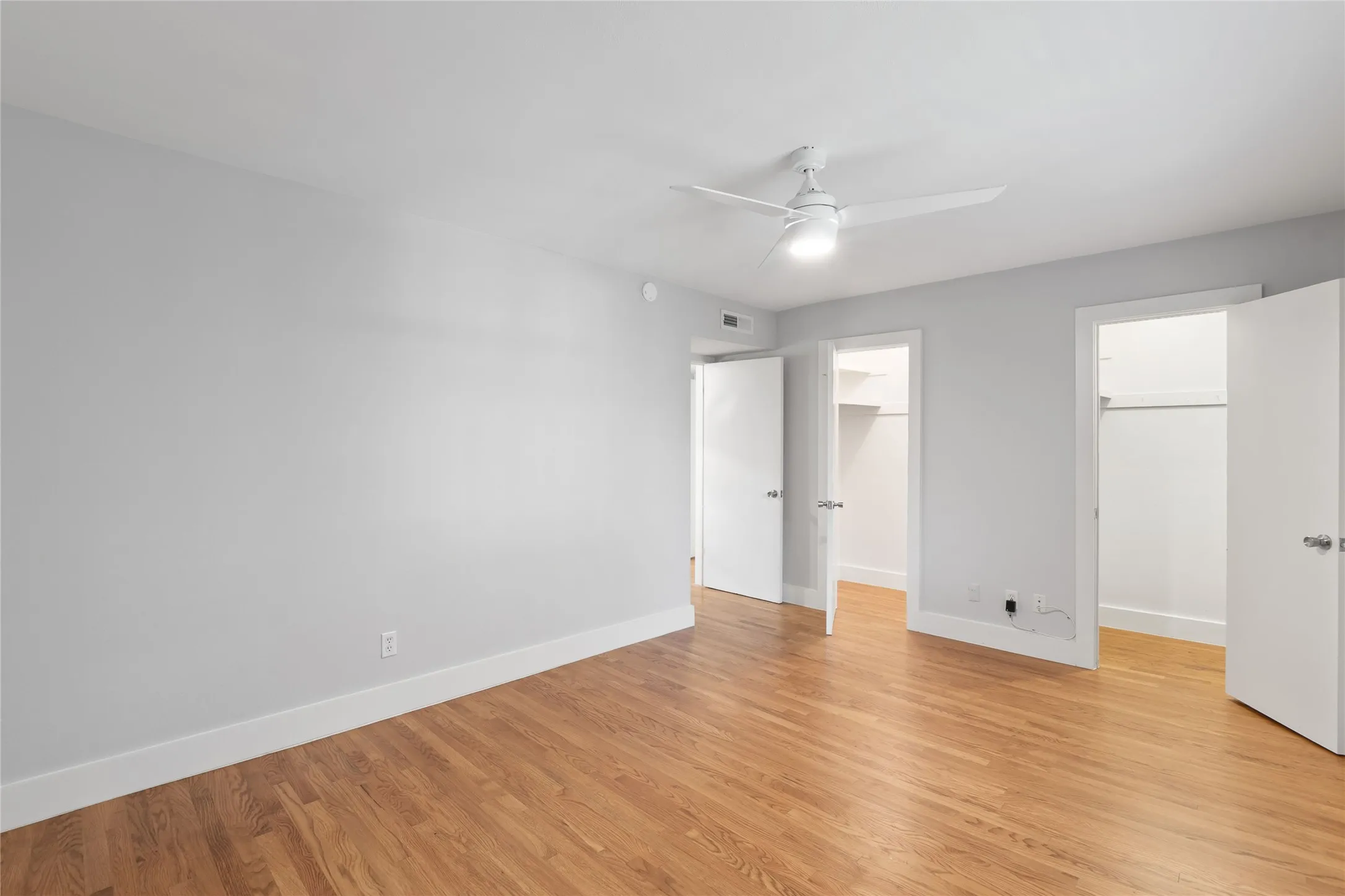 Unfurnished bedroom with a spacious closet, light wood-style flooring, and ceiling fan