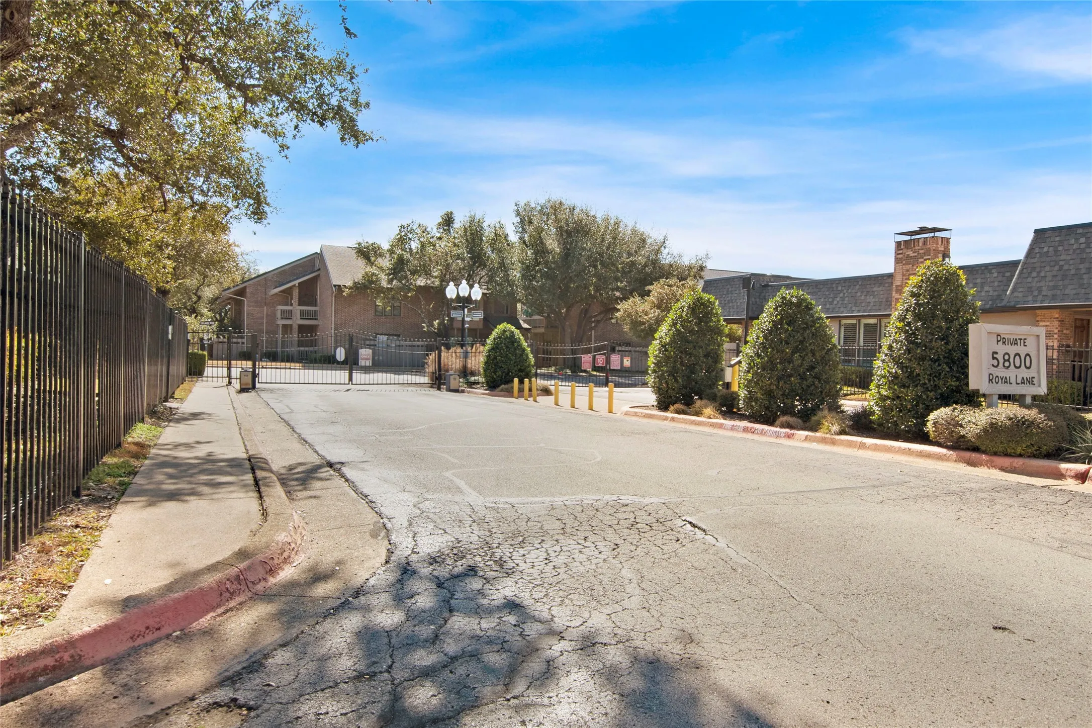 View of asphalt road featuring curbs, a gated entry, street lighting, sidewalks, and a residential view