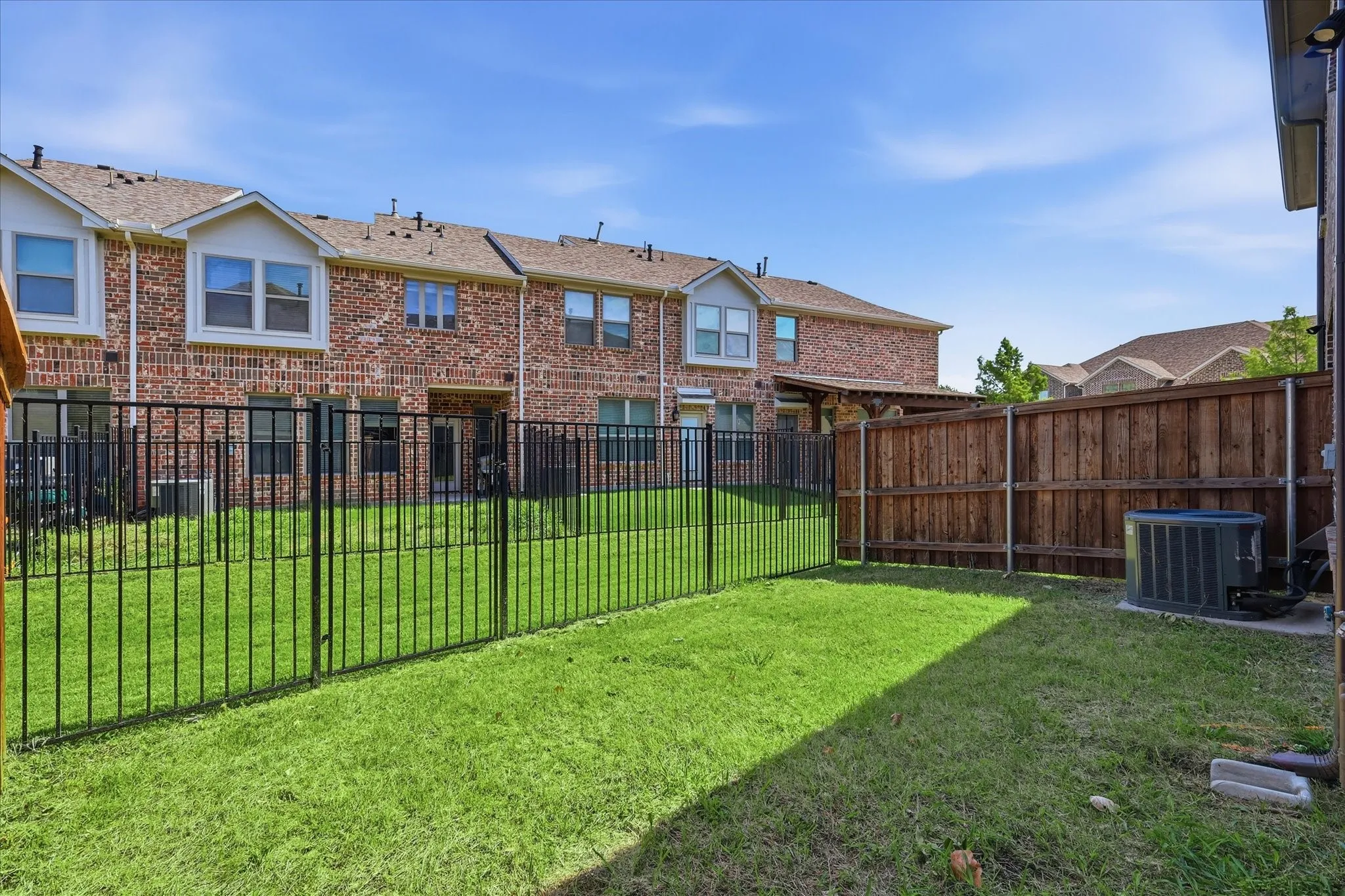 Private fenced backyard featuring a grassy area, wood privacy fence, and black metal fencing