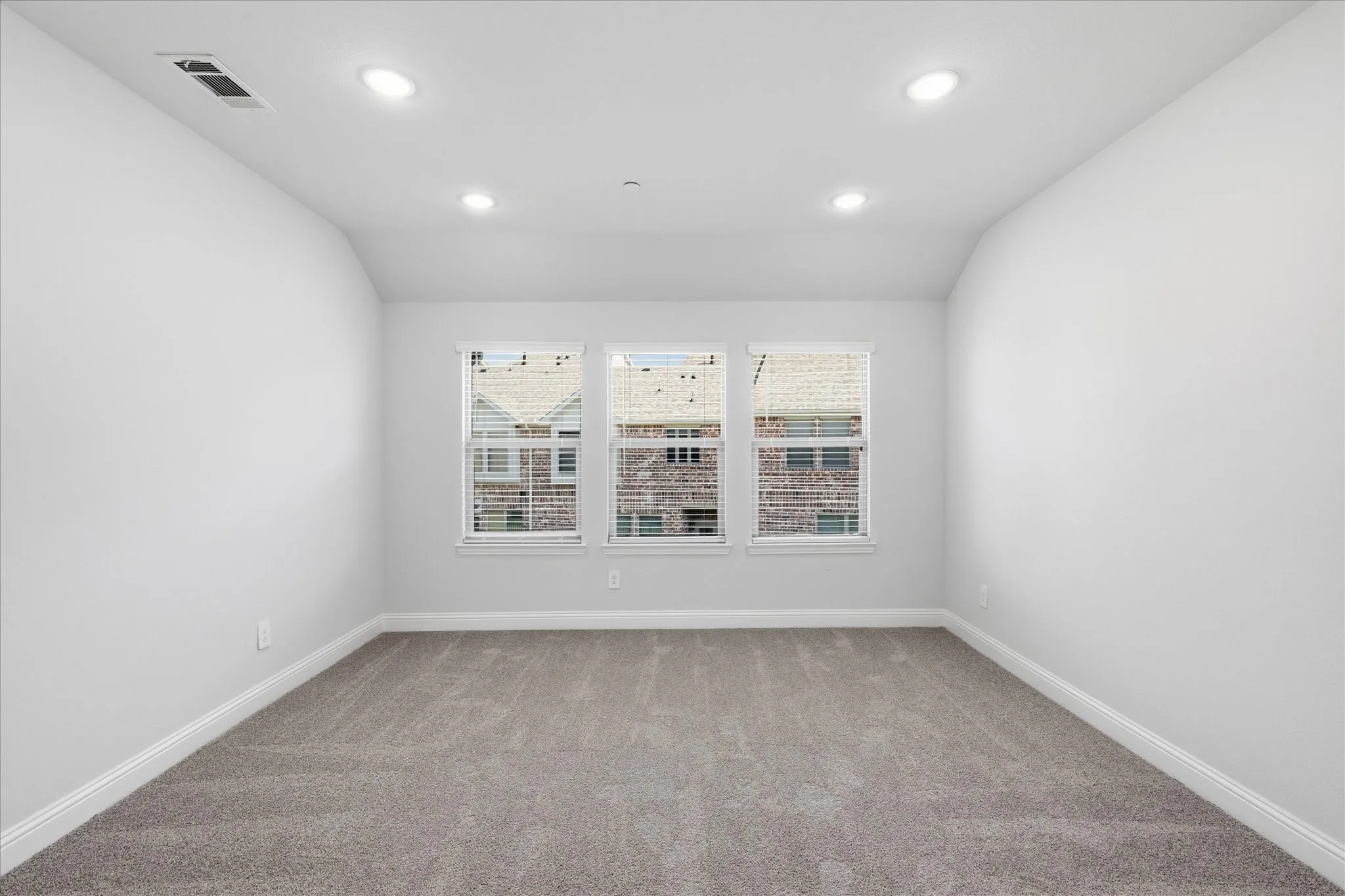 Neutral wall paint, gray carpeting, three windows with white blinds, and recessed ceiling lighting