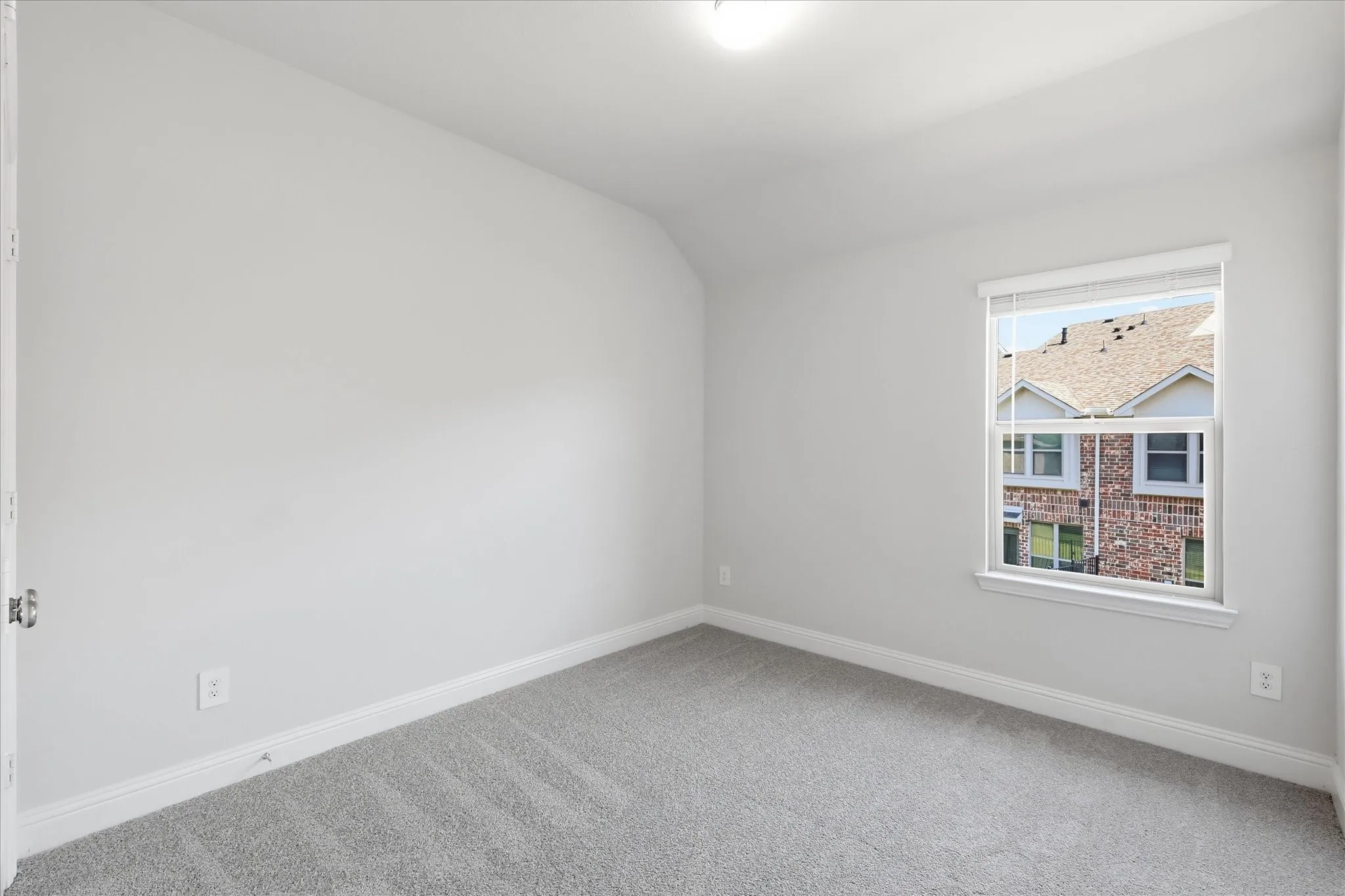 Neutral wall finishes, plush grey carpeting, and a single window with blinds