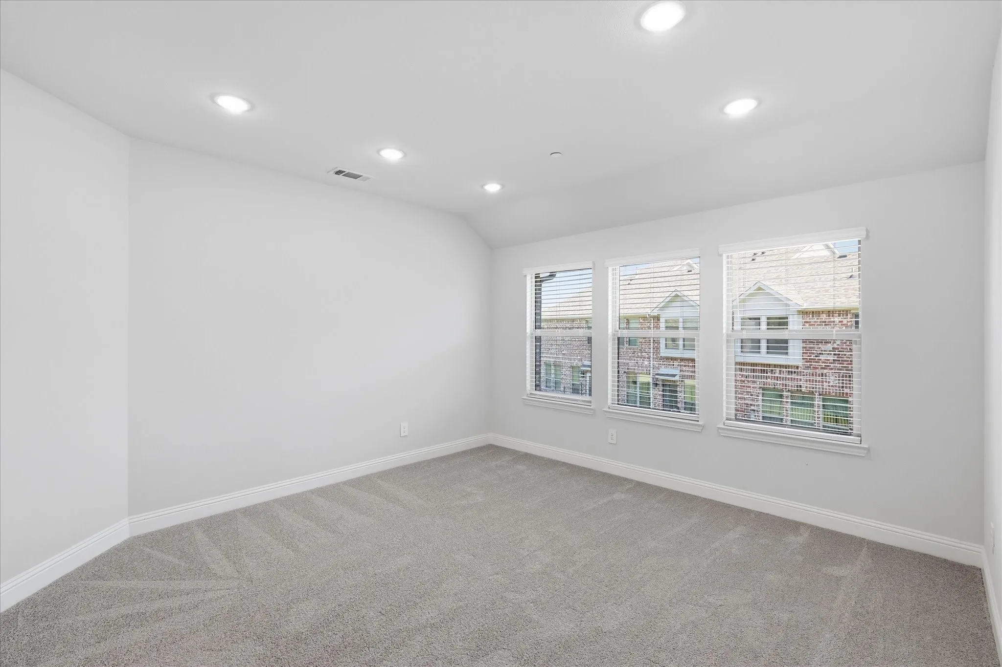 Recessed ceiling lighting, three windows with white blinds, light gray wall paint, and gray carpeted flooring