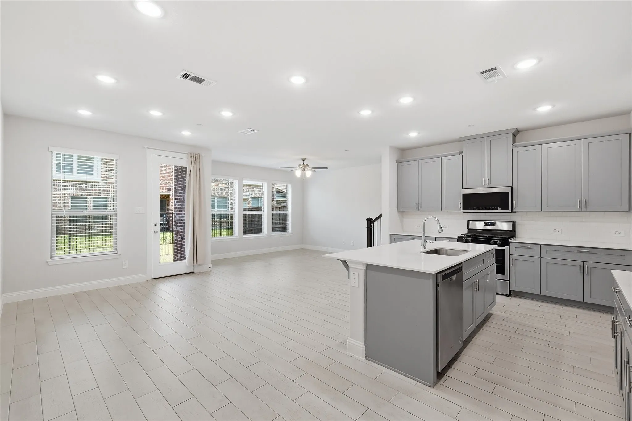 Spacious open-concept living area with light-toned tile flooring and recessed lighting