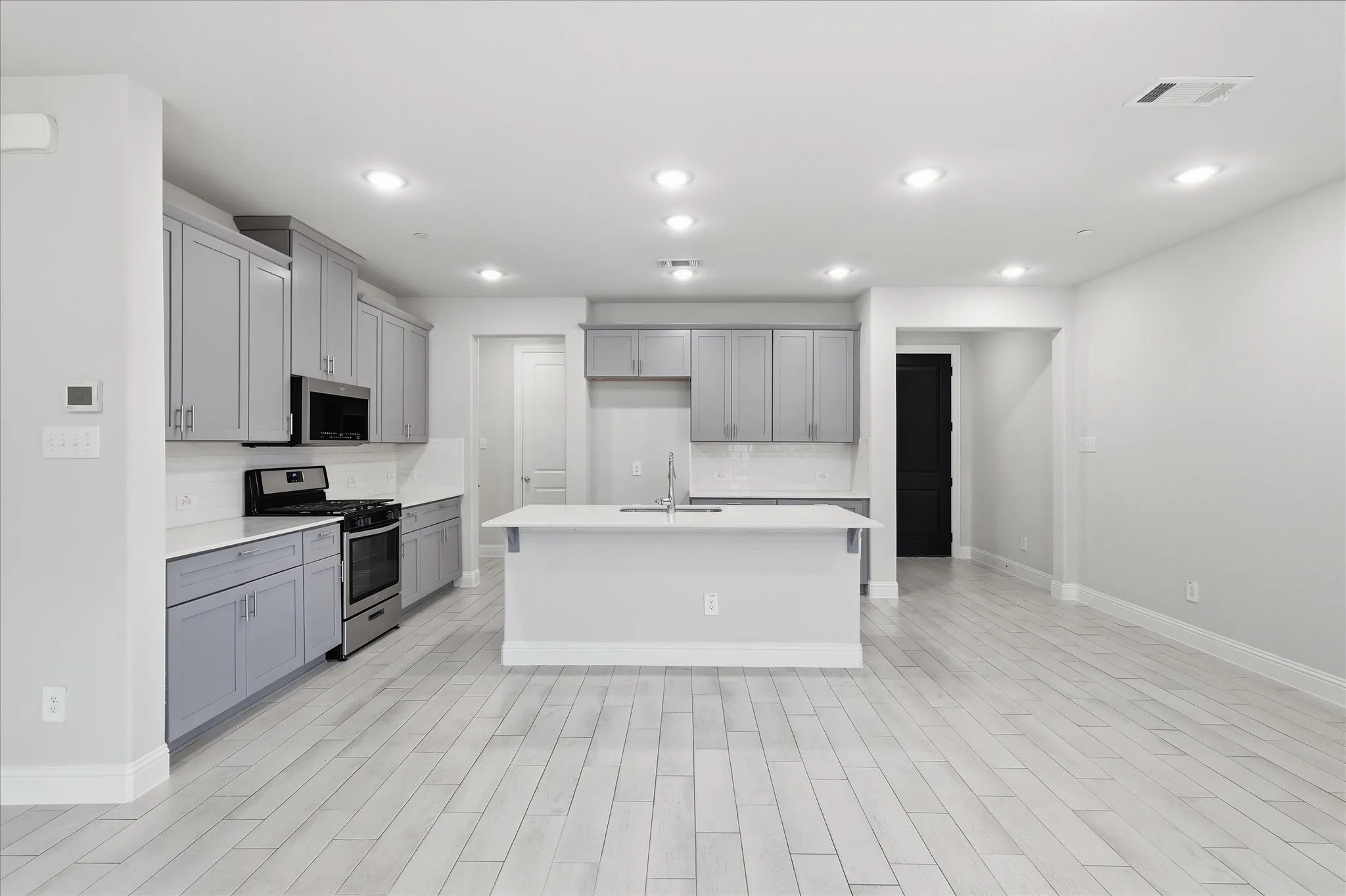 Modern kitchen featuring light gray cabinetry, stainless steel appliances, a center island with sink, white countertops, and wood-finish flooring