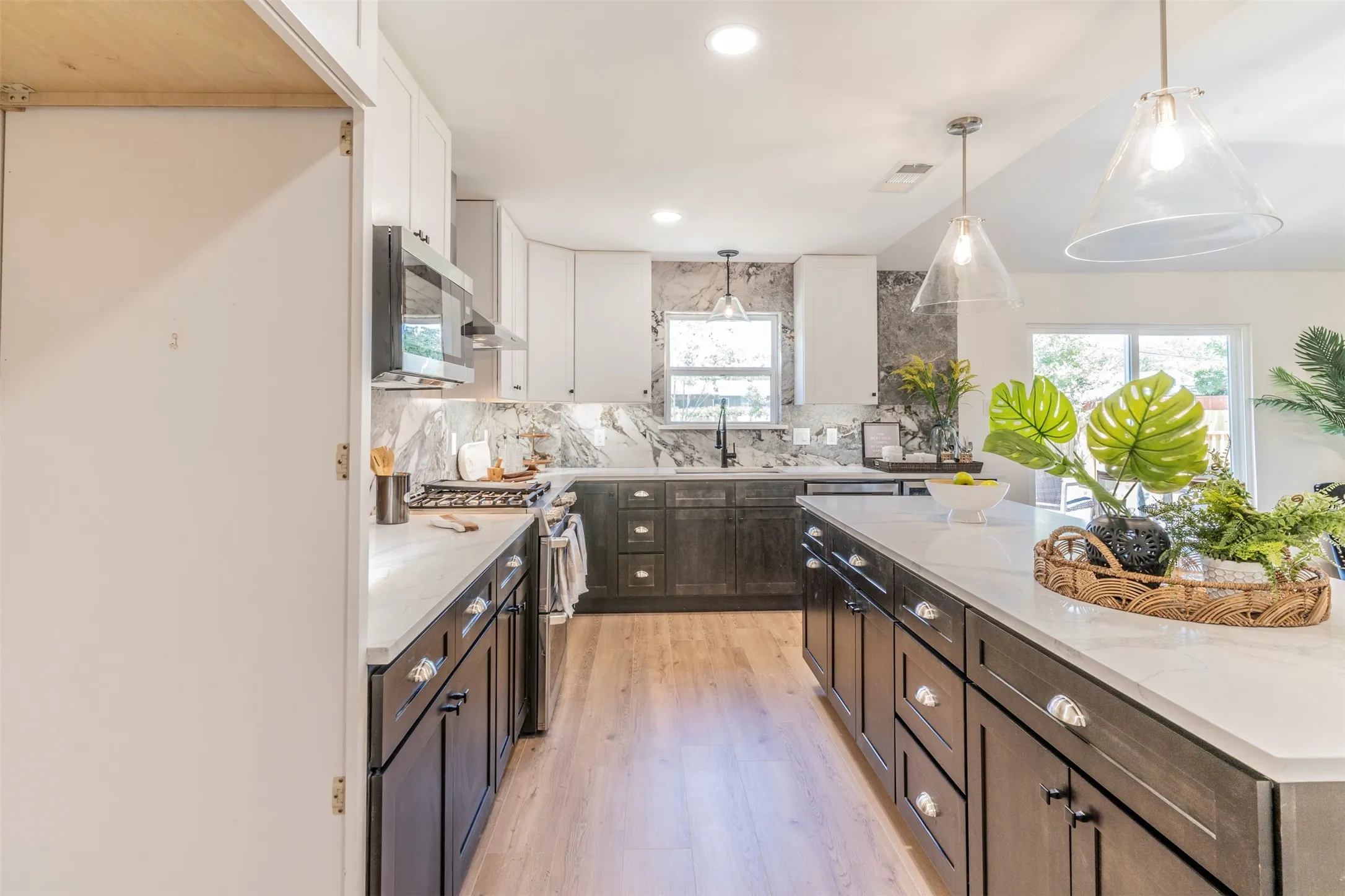 Kitchen featuring light wood-finish flooring, two-tone cabinetry with white upper and dark lower cabinets, a central island with white countertop, and pendant lighting