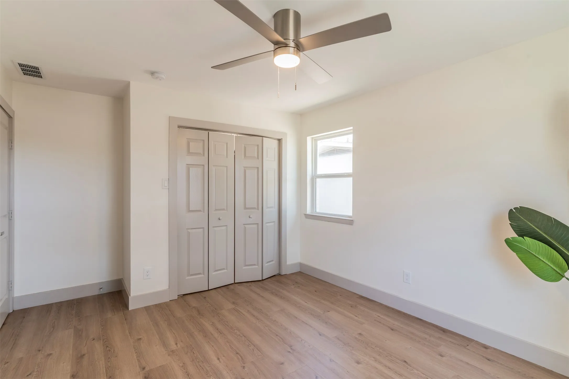 Wood-finish flooring, ceiling fan with integrated lighting, bi-fold closet doors, and single-pane window