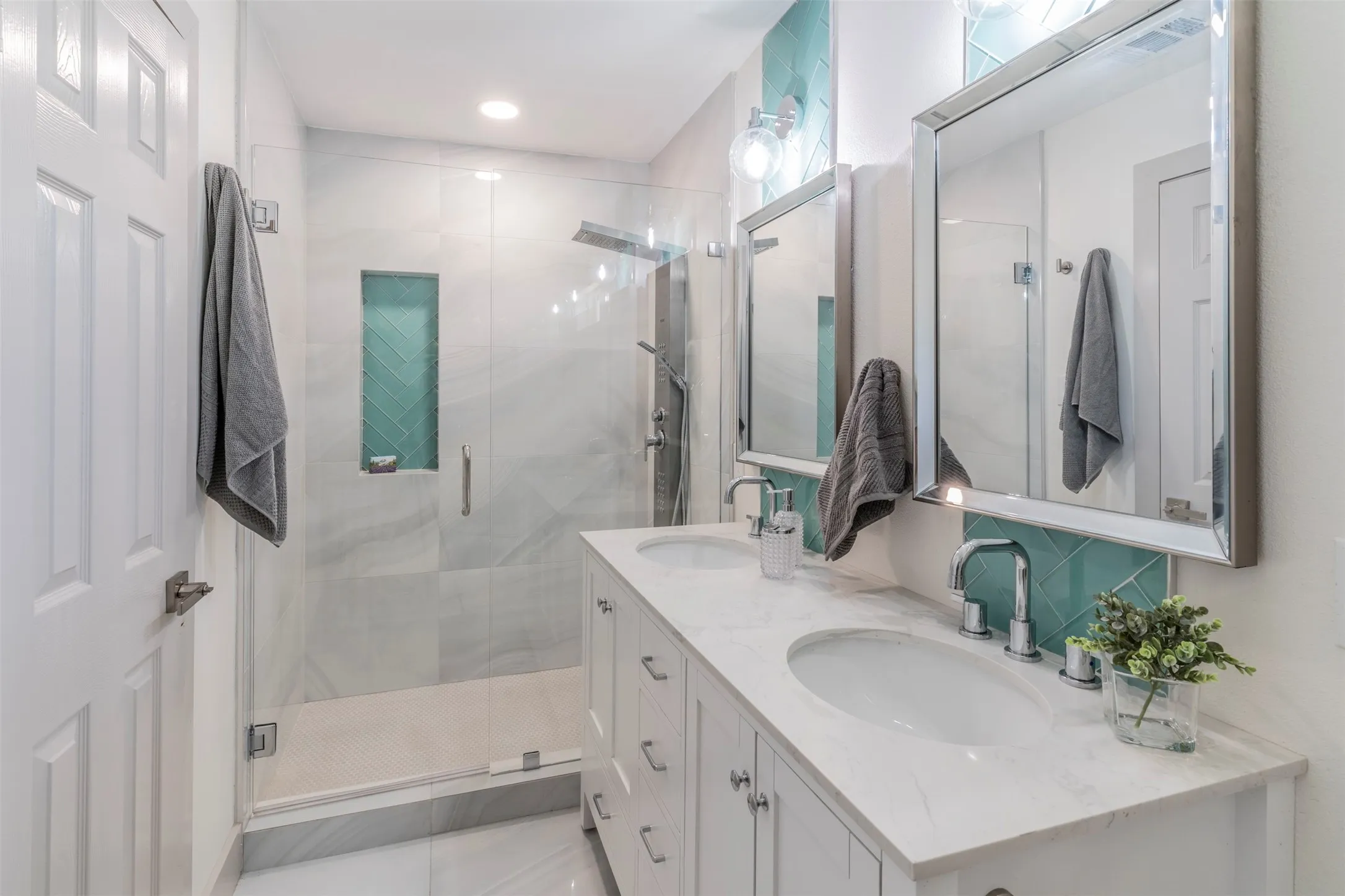 Dual vanity with white cabinetry and integrated sinks, glass-enclosed shower with a built-in niche, and a tiled shower surround