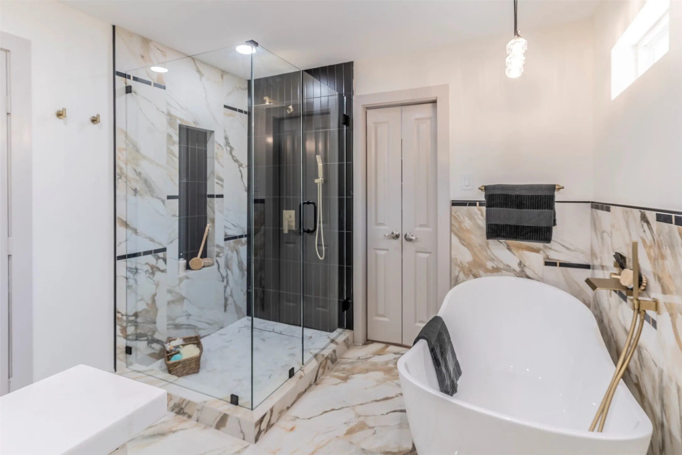 Freestanding soaking tub with gold-finish floor-mounted faucet, glass-enclosed shower with tile surround, and marble-finish tile flooring