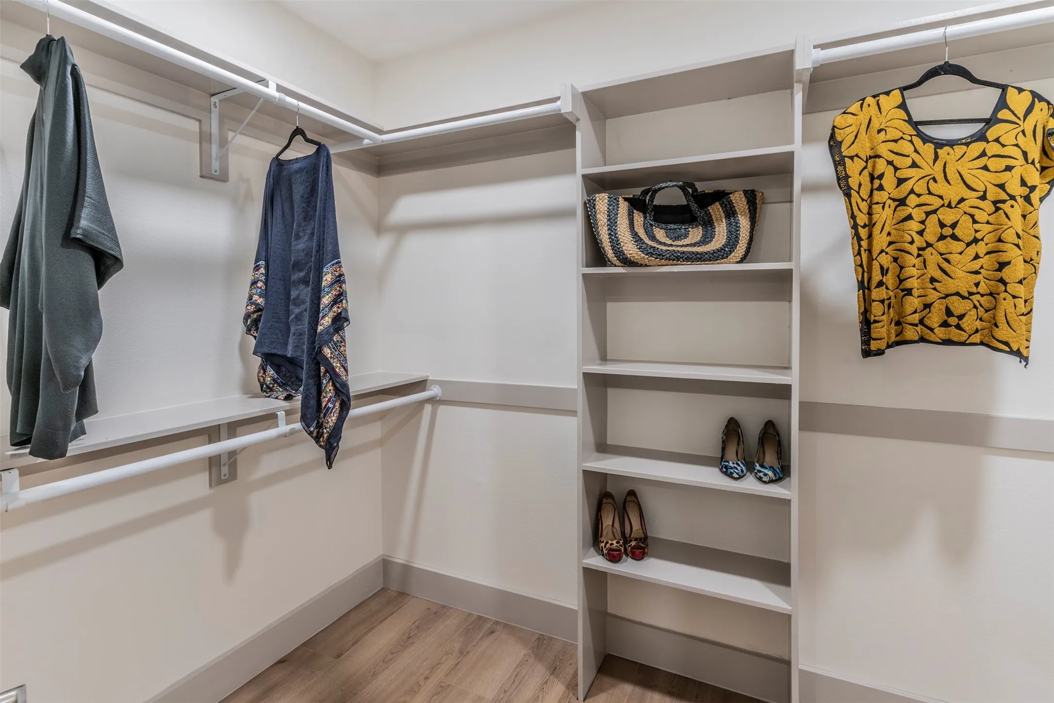 Built-in closet system featuring multiple hanging rods, corner shelving, and wood-finish flooring