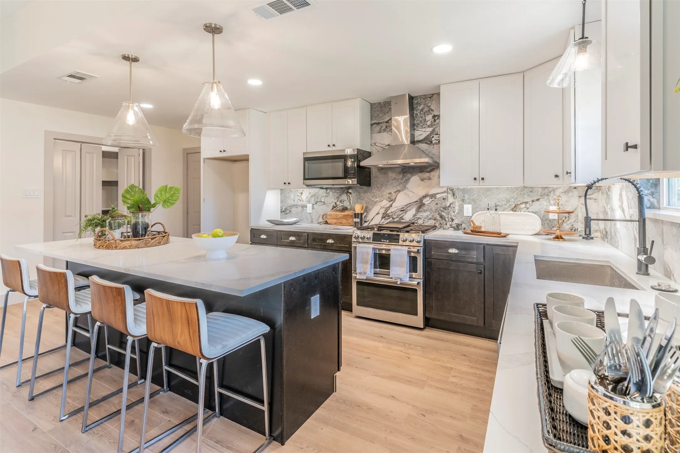 Kitchen featuring an expansive island with seating, stainless steel appliances, a built-in microwave, a range hood, and wood-finish flooring
