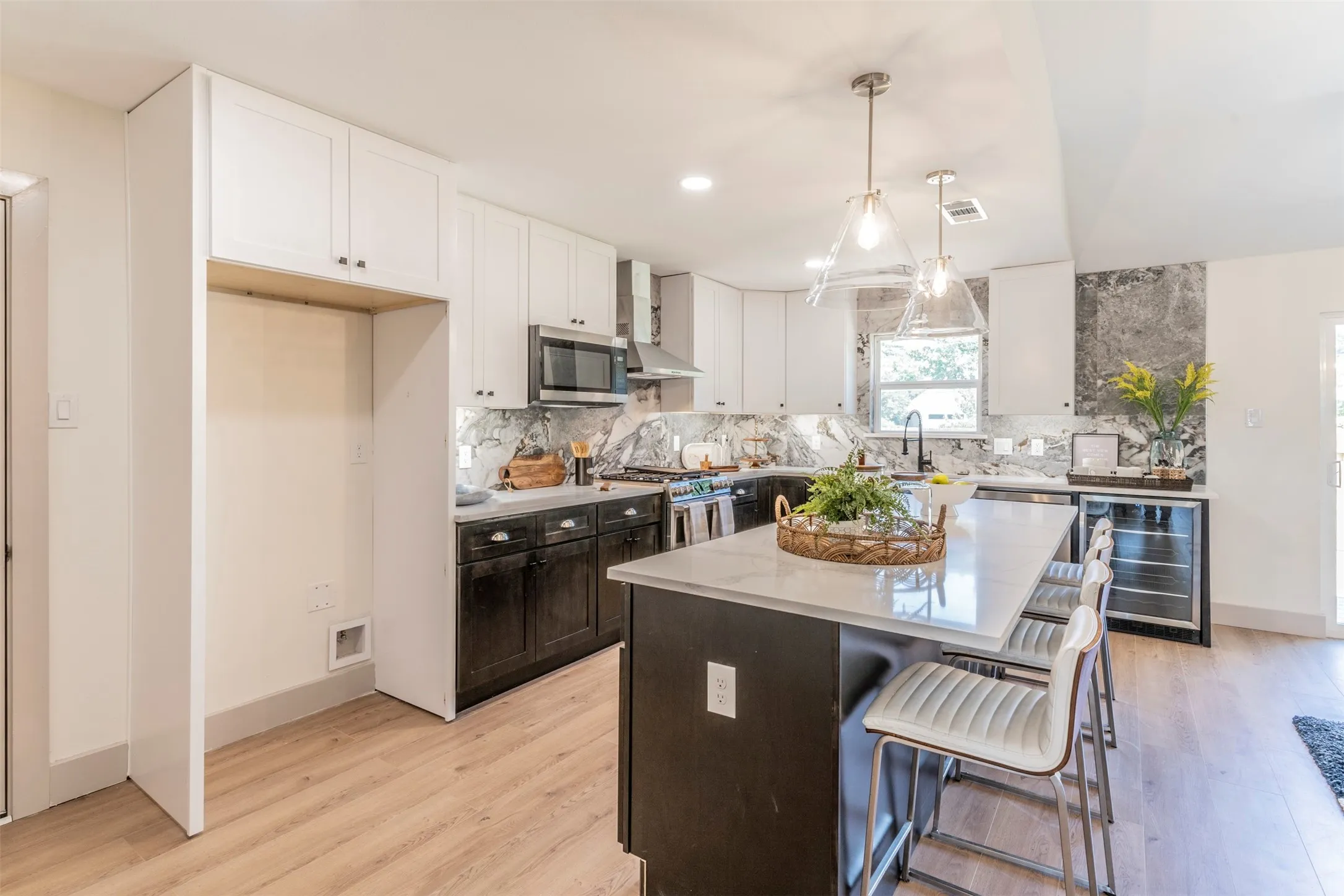 Kitchen featuring light-finish flooring, an island with a light-toned countertop, a built-in beverage cooler, and white upper cabinetry with dark lower cabinetry
