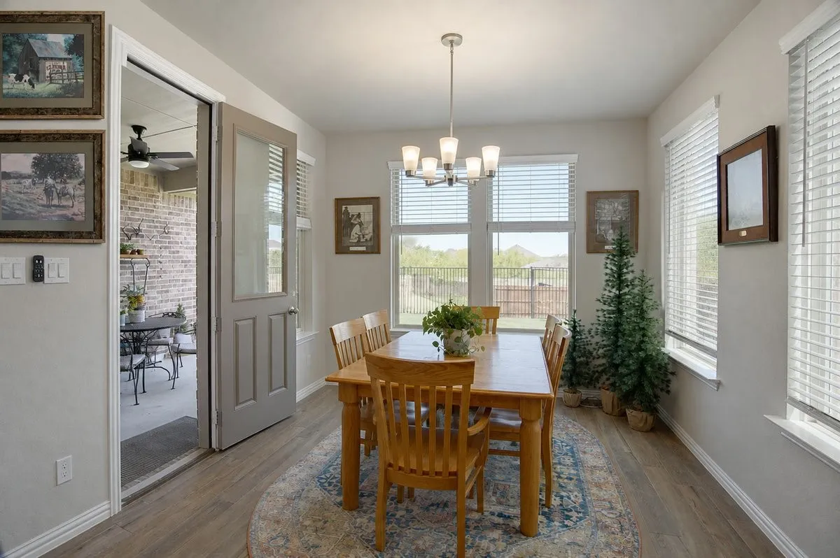 Dining area with wood-finish flooring, a contemporary chandelier, multiple windows, and a glass-paneled door leading to an outdoor space