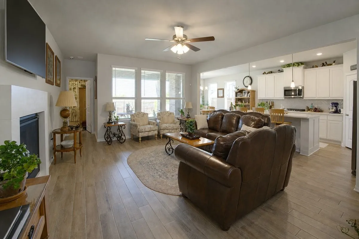 Spacious living area featuring wood-finish flooring, a ceiling fan, and multiple windows