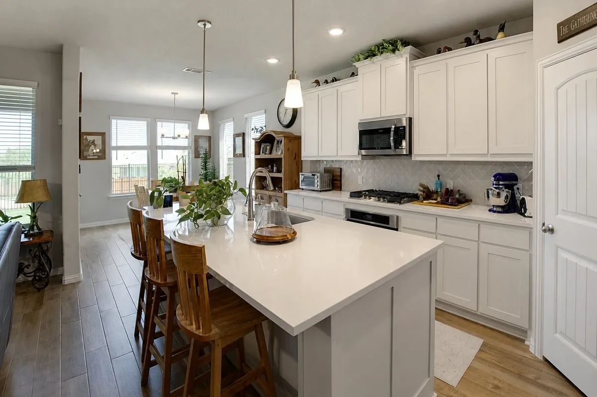 Kitchen featuring a large island with a surface, white cabinetry, stainless steel appliances, a tile backsplash, and wood-finish flooring