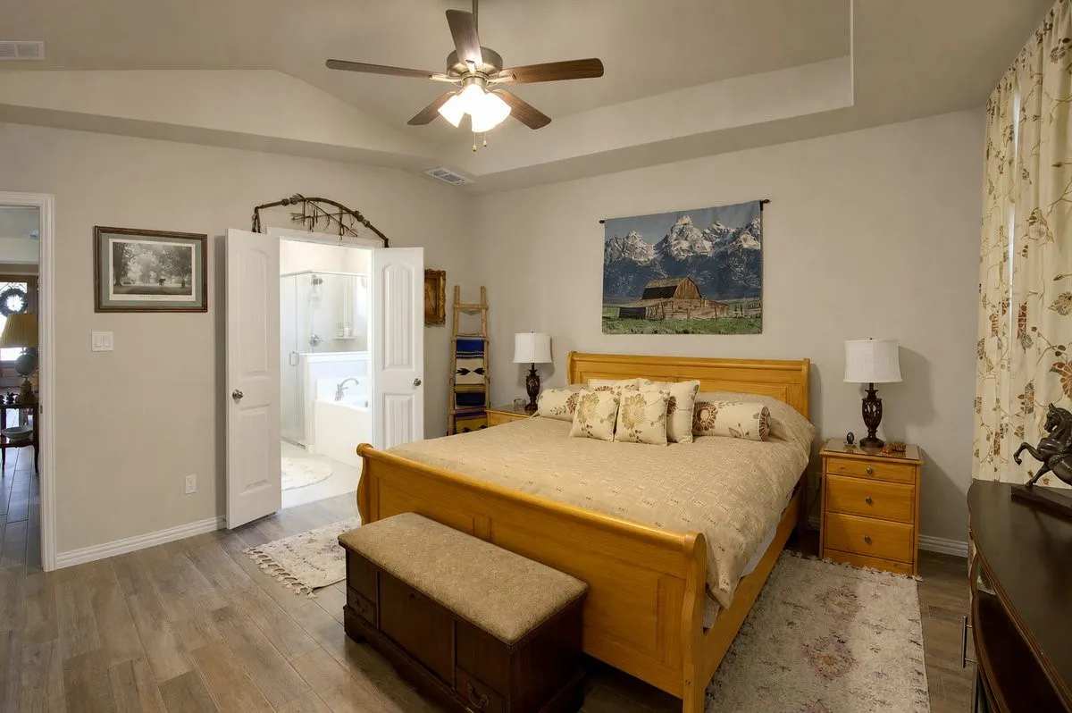 Tray ceiling with a ceiling fan, wood-finish flooring, double doors leading to a bathroom, and light-toned walls