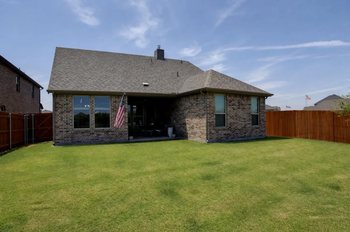 Brick exterior with a covered patio, fenced yard, and a shingle roof