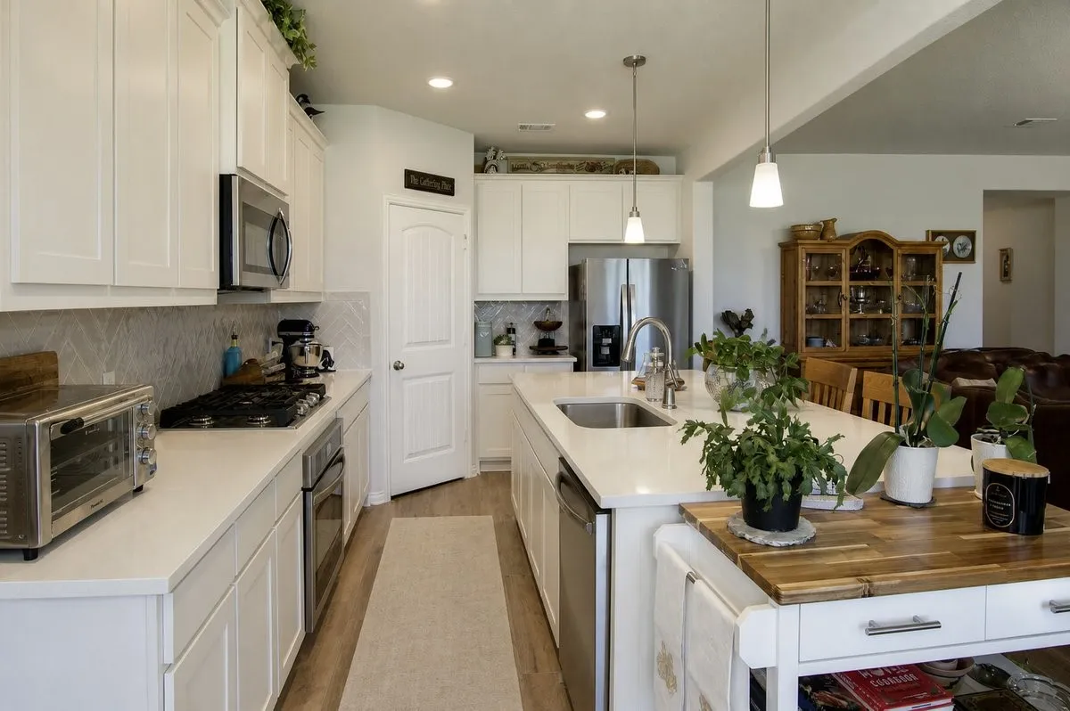 White shaker-style cabinetry, stainless steel appliances, recessed lighting, wood-finish flooring, and a kitchen island with an integrated sink