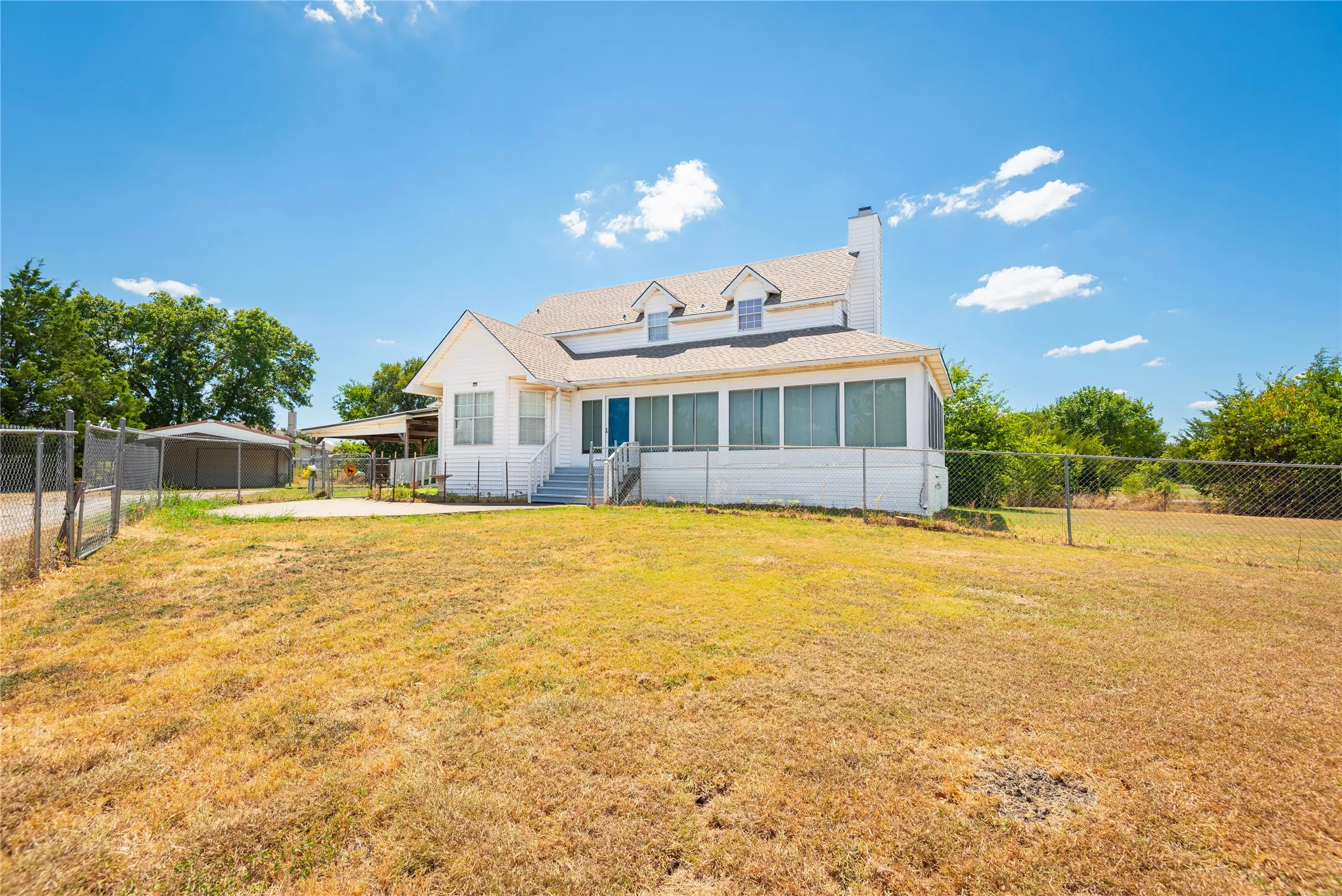 White single-story exterior with dormer windows, screened porch, and a chain-link fence