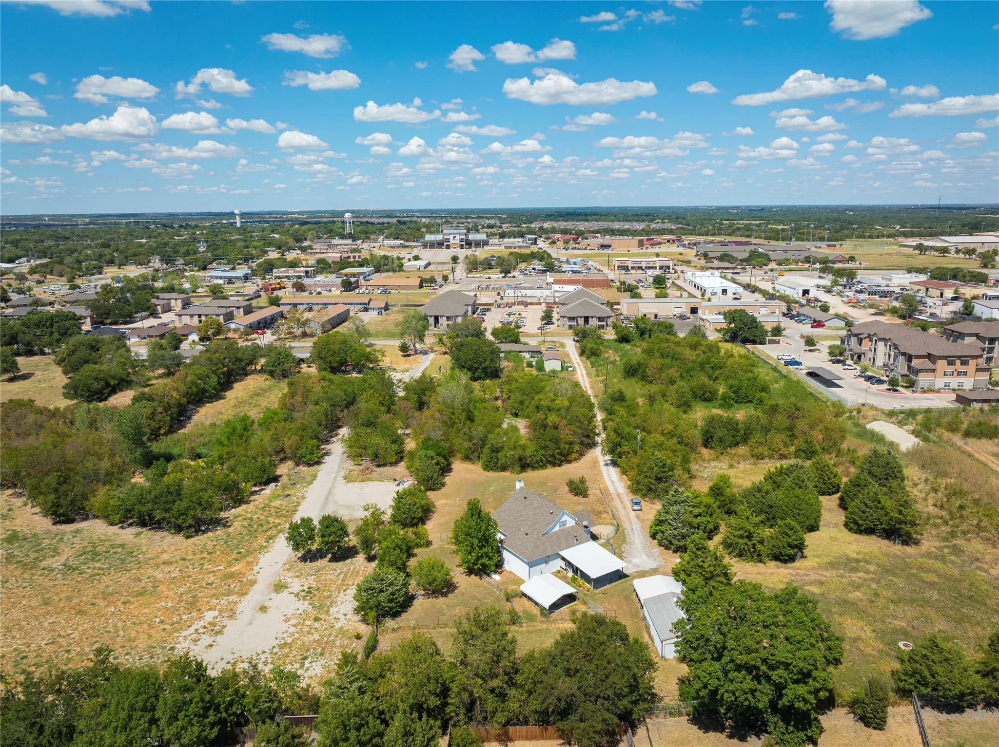 Expansive property featuring a single-story residence, multiple outbuildings, and a surrounding landscape with mature trees and open areas