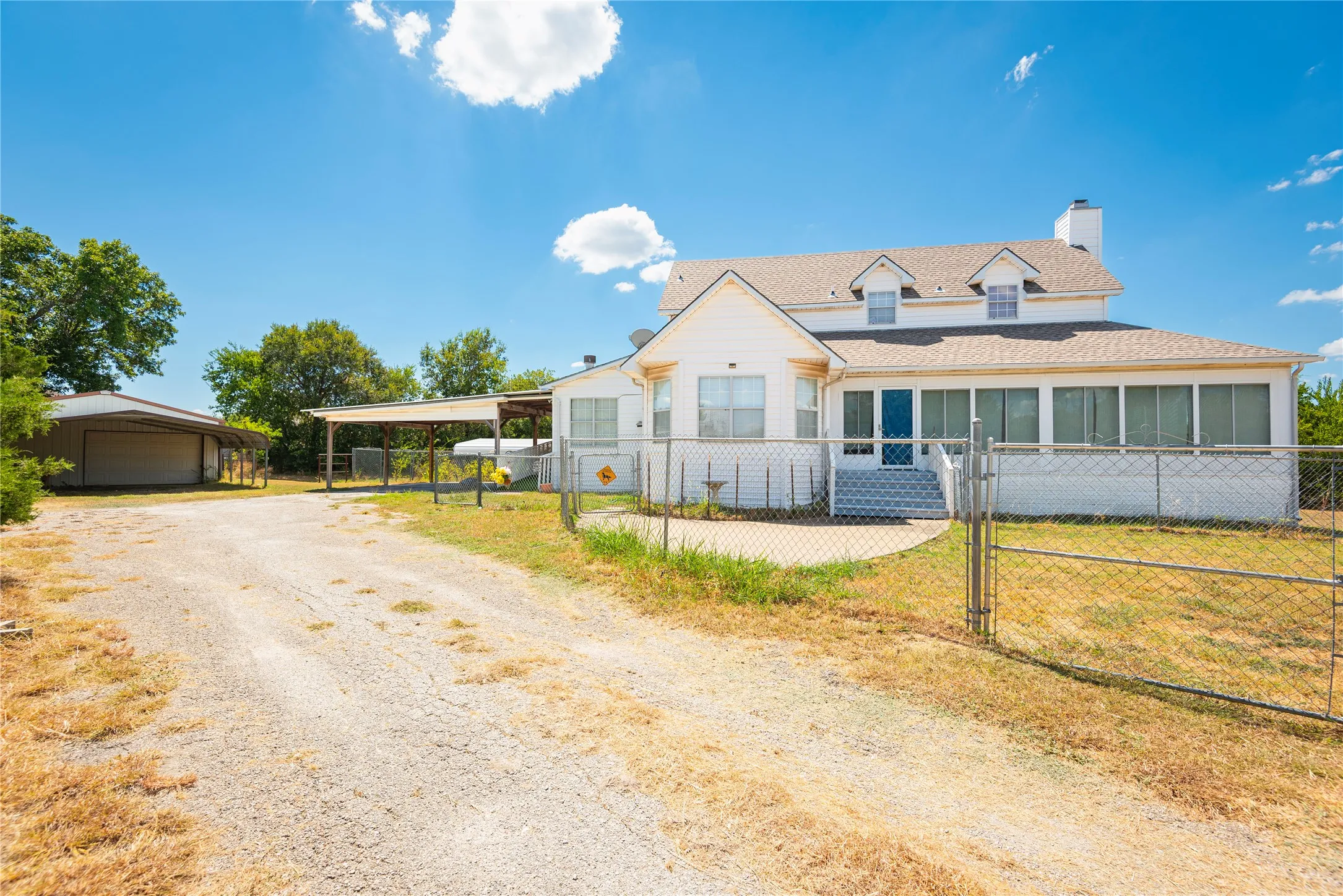White exterior with dormer windows, screened porch, attached carport, detached garage, and fenced yard