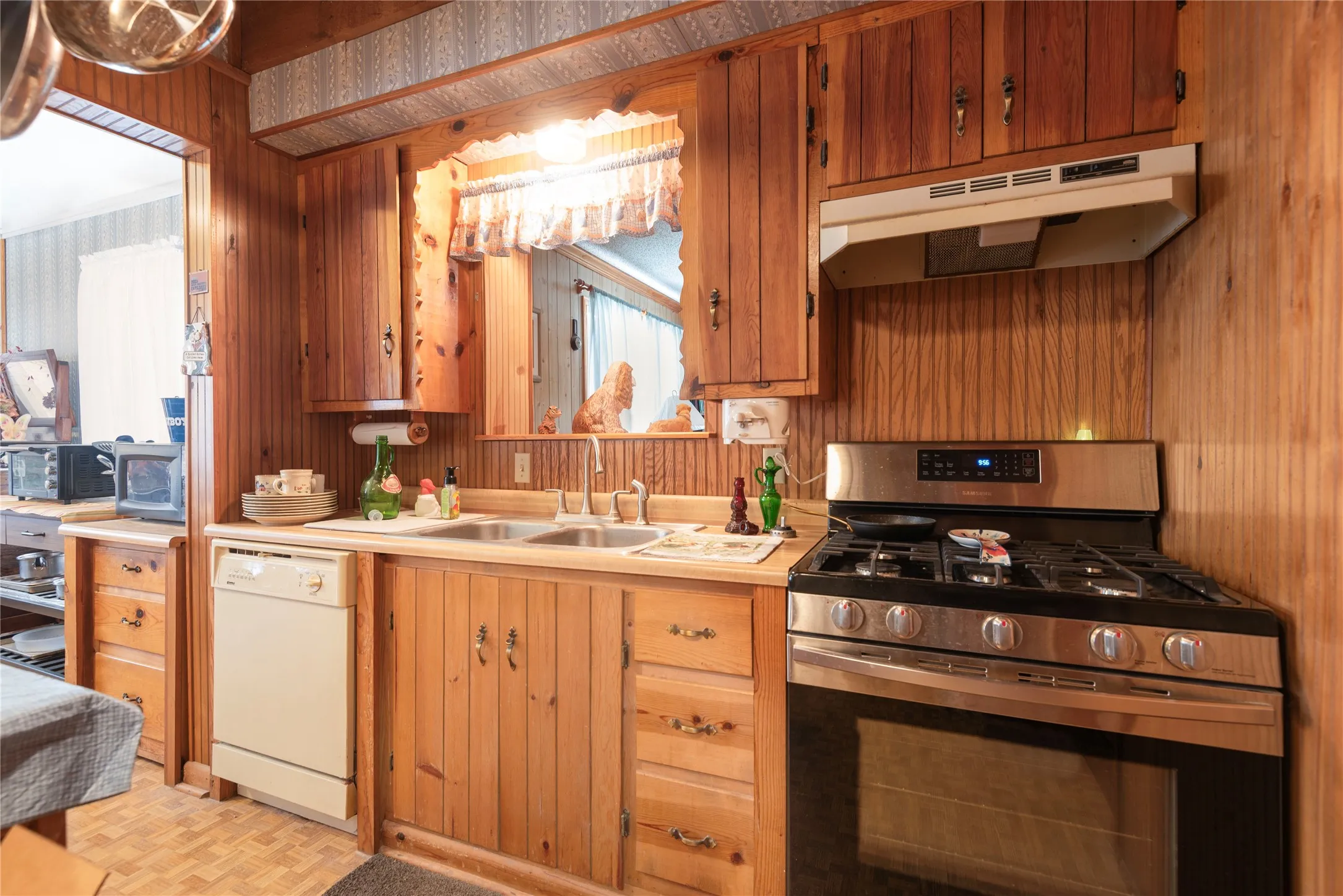 Wood-paneled kitchen featuring abundant wood cabinetry, stainless steel gas range, and a built-in dishwasher