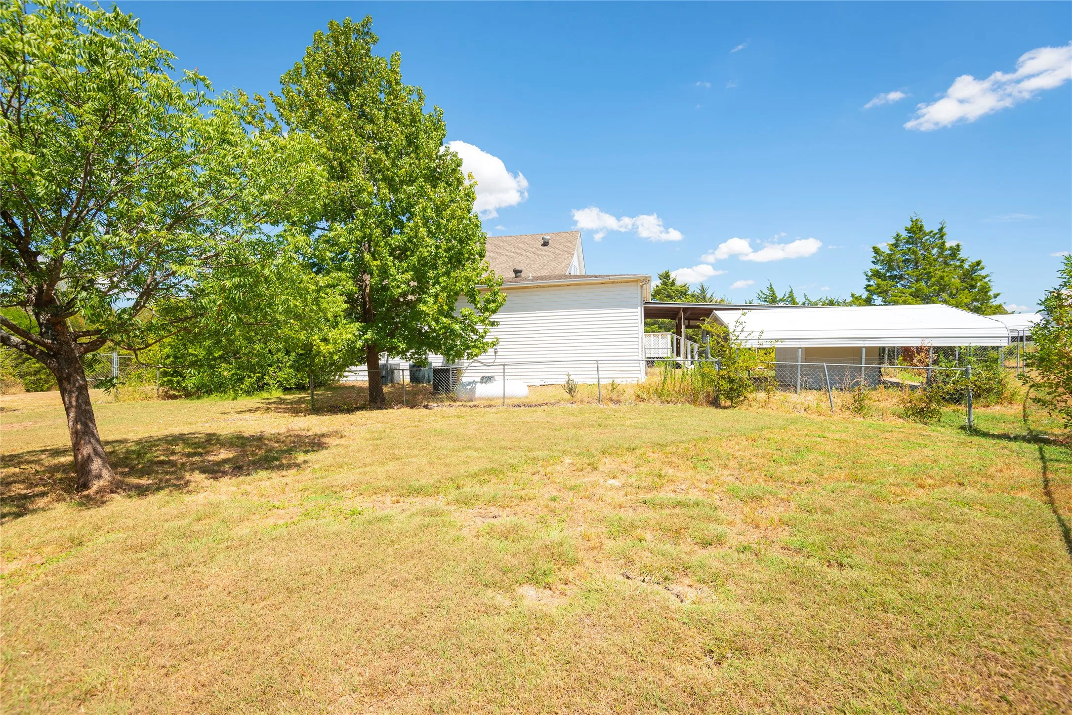 Expansive grassy area featuring mature trees and partial fencing