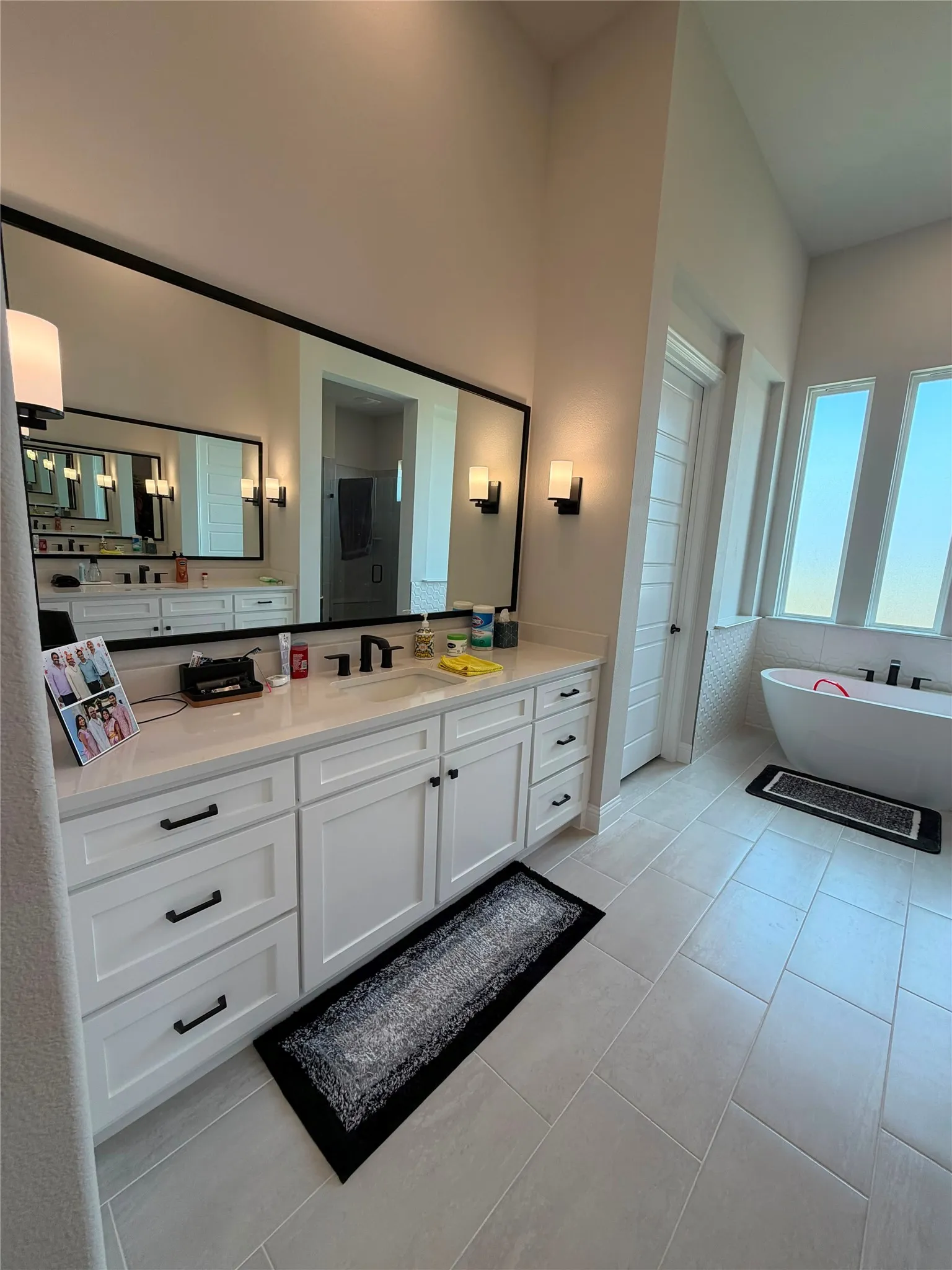 Dual vanity with white cabinetry, matte black hardware, and an expansive wall-mounted mirror