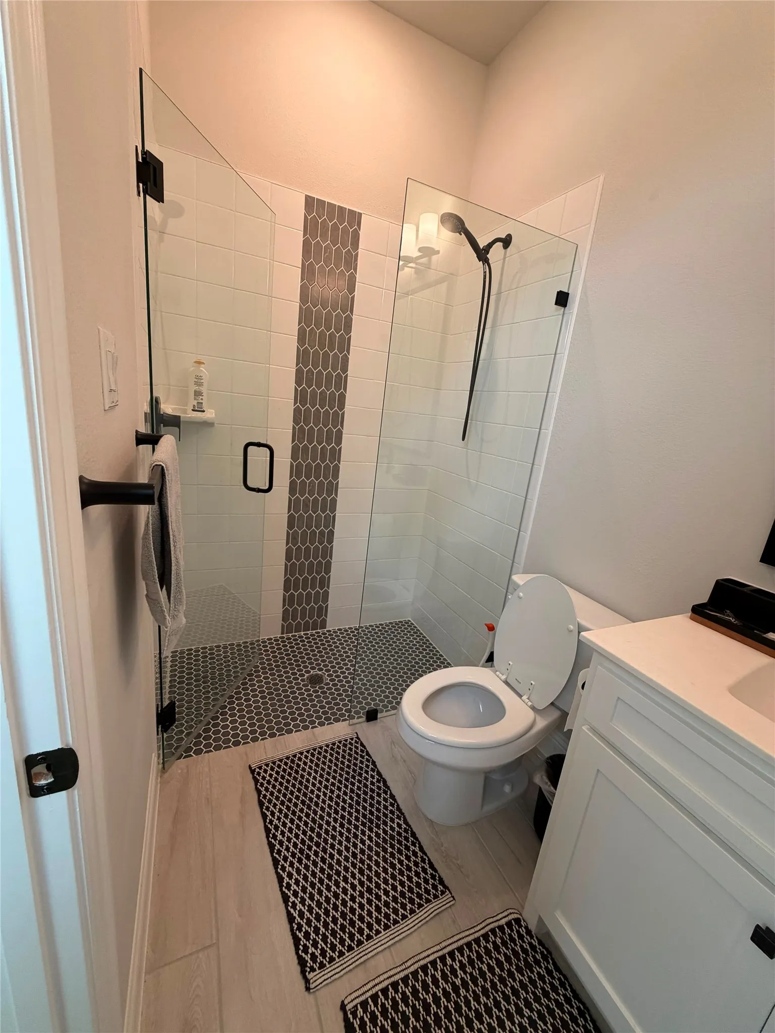 Walk-in shower with clear glass enclosure and black hardware, featuring a decorative vertical tile accent