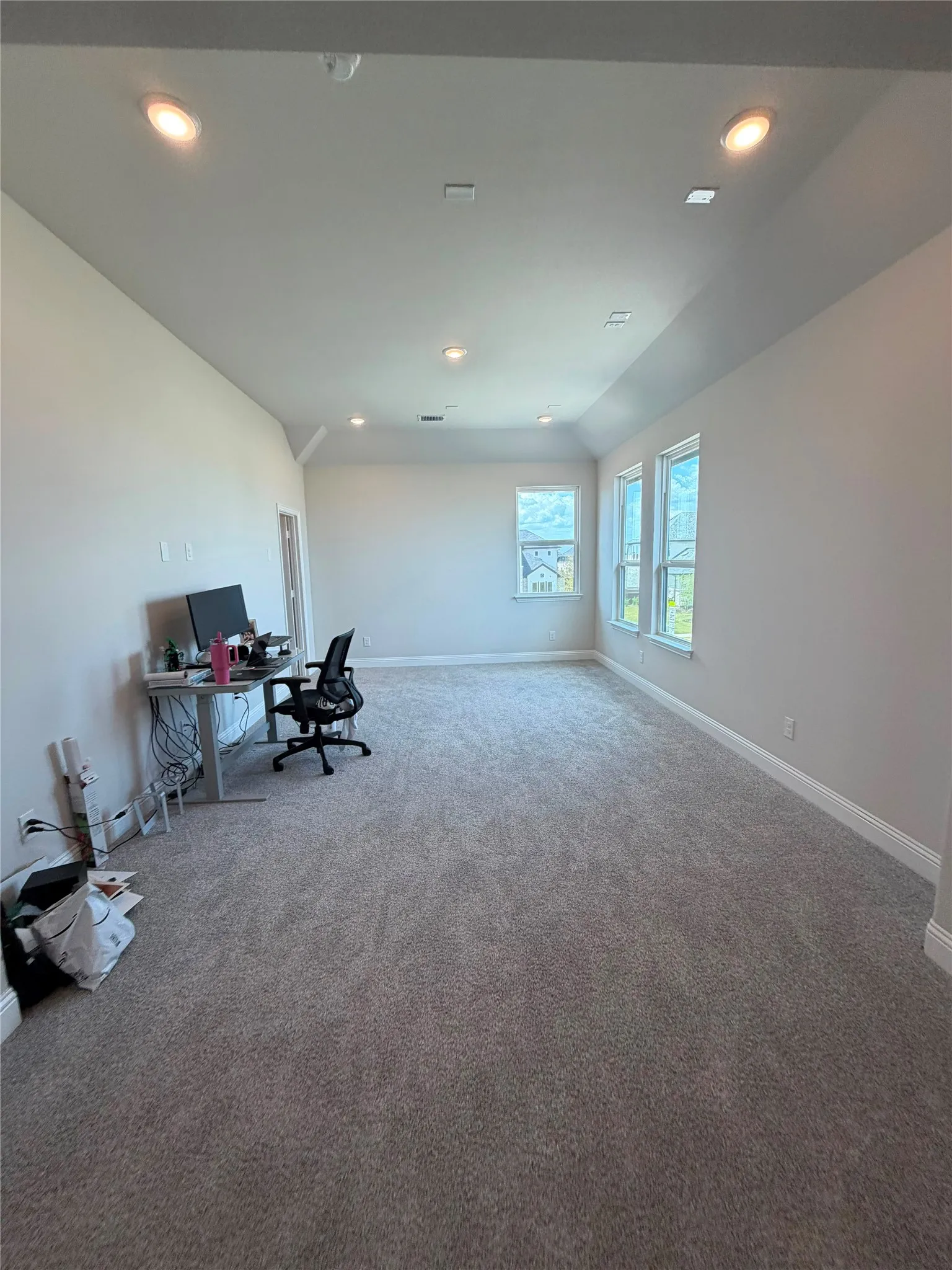 Recessed lighting, soft gray wall paint, multiple windows, and gray carpeted flooring