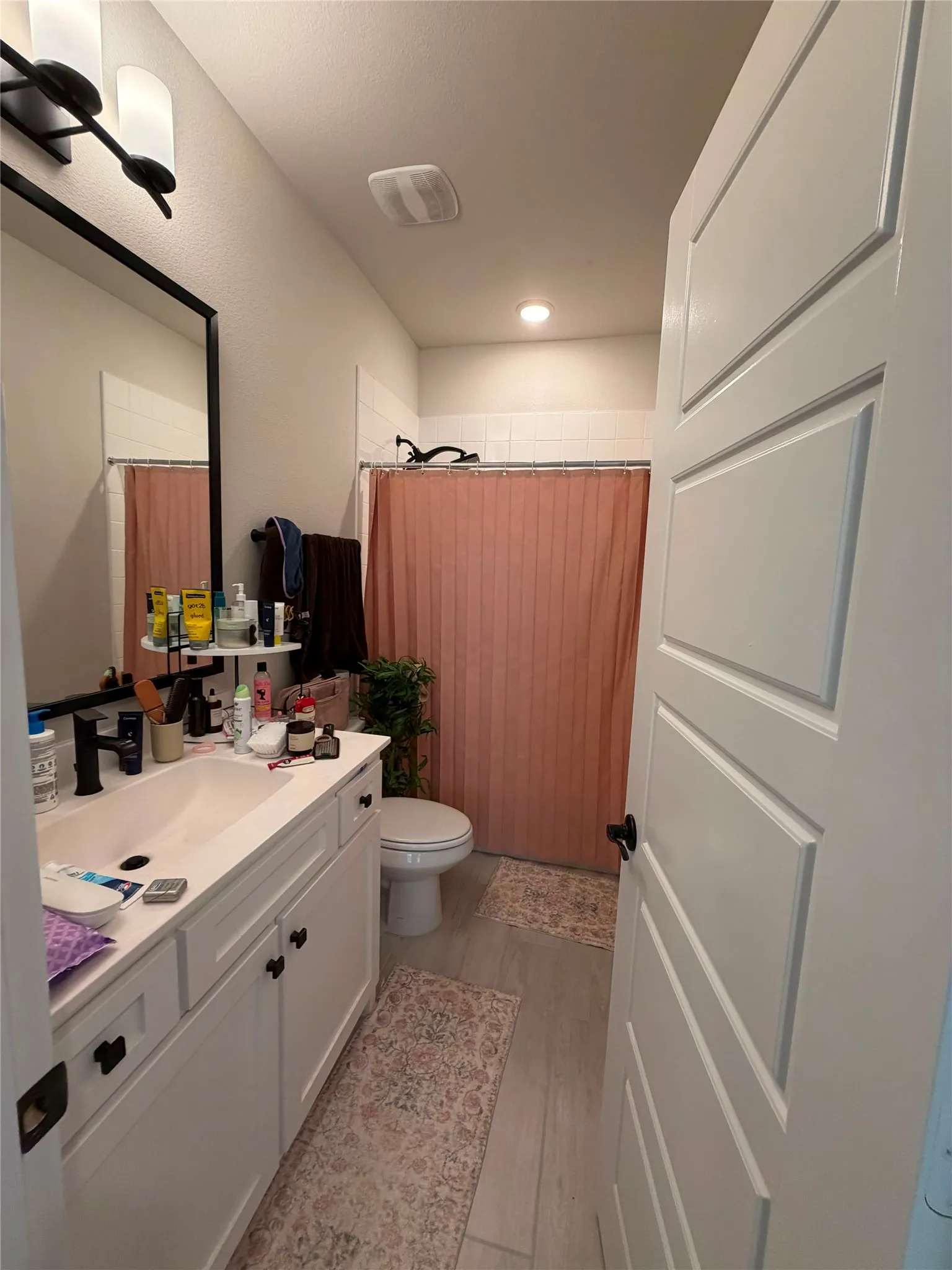 White paneled door with matte black hardware, white vanity with integrated sink, black-finish faucet, and coordinating overhead lighting