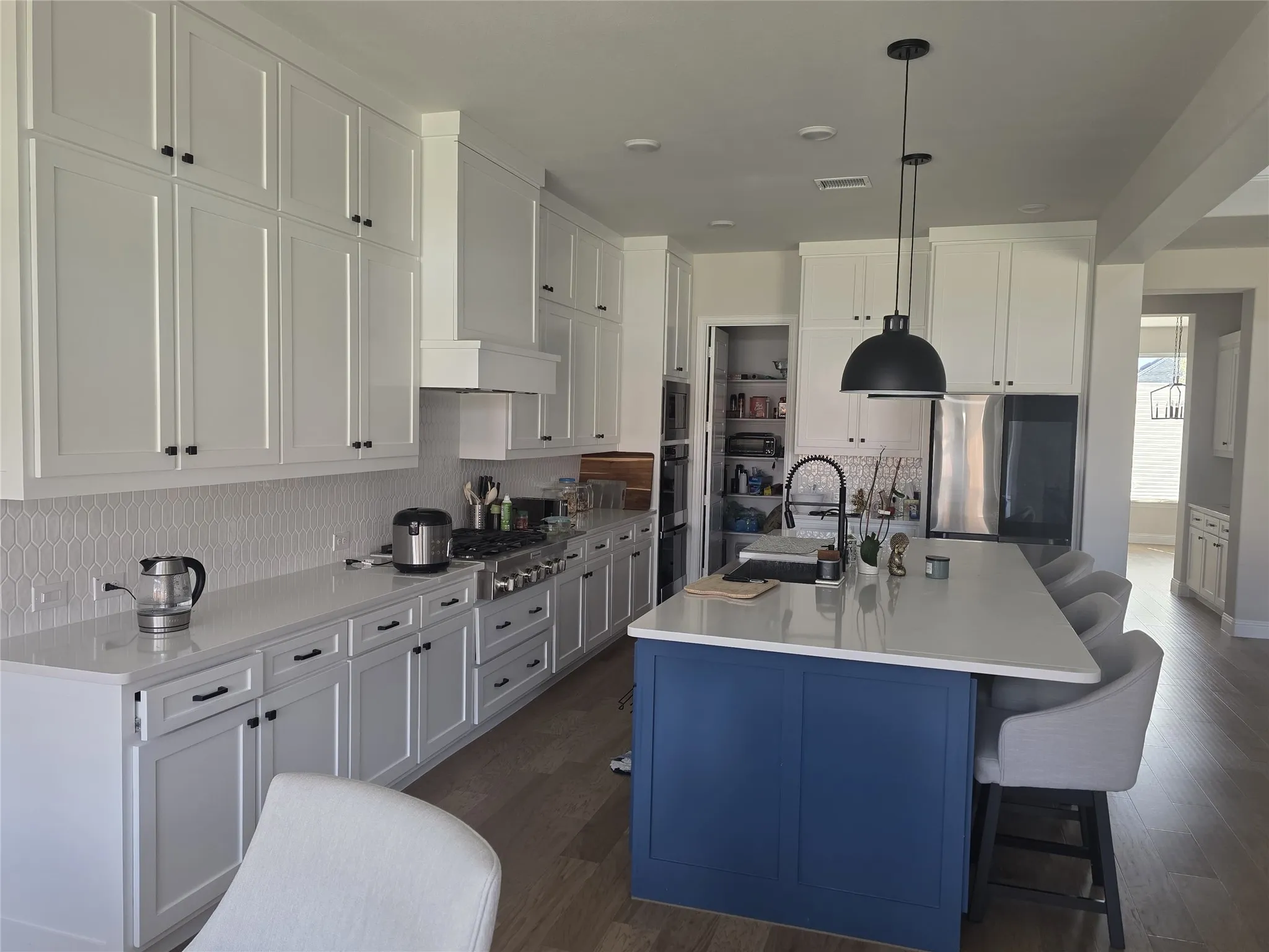 Gourmet kitchen with extensive white cabinetry, light-toned countertops, a contrasting blue island, stainless steel appliances, and wood-finish flooring
